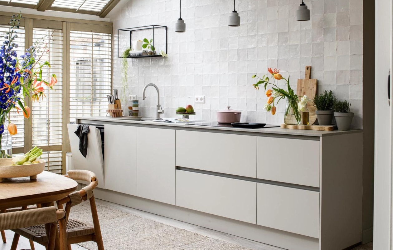 Verf muren Zandsteenbruin Flexa, wandtegels vtwonen tegels by Douglas &amp; Jones: Craft Egg White glossy decor 12,5×12,5 cm Douglas, PVC-vloer met vloerverwarming Woninginrichting-Aanhuis.nl, houten shutters op maat gemaakt, in de kleur old white Jasno, keuken van vtwonen in de kleur greige en kast (links naast de eettafel) onderdeel van de keuken Mandemakers, vloerkleed Hemp Eijerkamp, kunstwerk Ezel op het strand van Scheveningen, Anton Mauve uit de oude meesters collectie Werk aan de Muur, inductiekookplaat PVQ895F25E, compacte oven met magnetron CMG8764C7 en stoomoven HSG836NC1 Bosch, hanglampen, tafellamp en klok Zuiver, taartschaal, mokken en marmeren serveerplank van HKliving, roze braadpan van BK Bourgogne. Overig privébezit Weer verliefd op je huis, aflevering 11 seizoen 17 | styling Fietje Bruijn | fotografie Margriet Hoekstra
