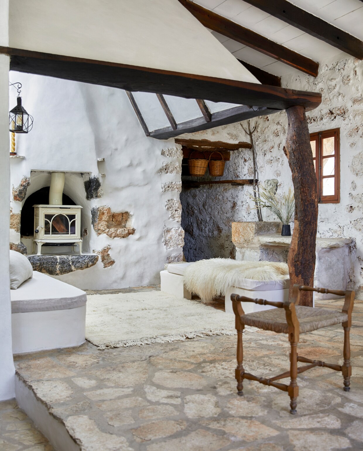 Op de ingebouwde banken liggen schapenvachten uit Ierland. Houtkachel Jotul. De originele muren zijn deels afgewerkt met tadelakt. Vloerkleed uit Marokko. Stoel en wandlamp waren al in het huis. Manden lokaal gekocht. Vaas uit eigen atelier. vtwonen special binnenkkijken 06-2023 | productie Bureaux/Living Inside | fotografie Greg Cox