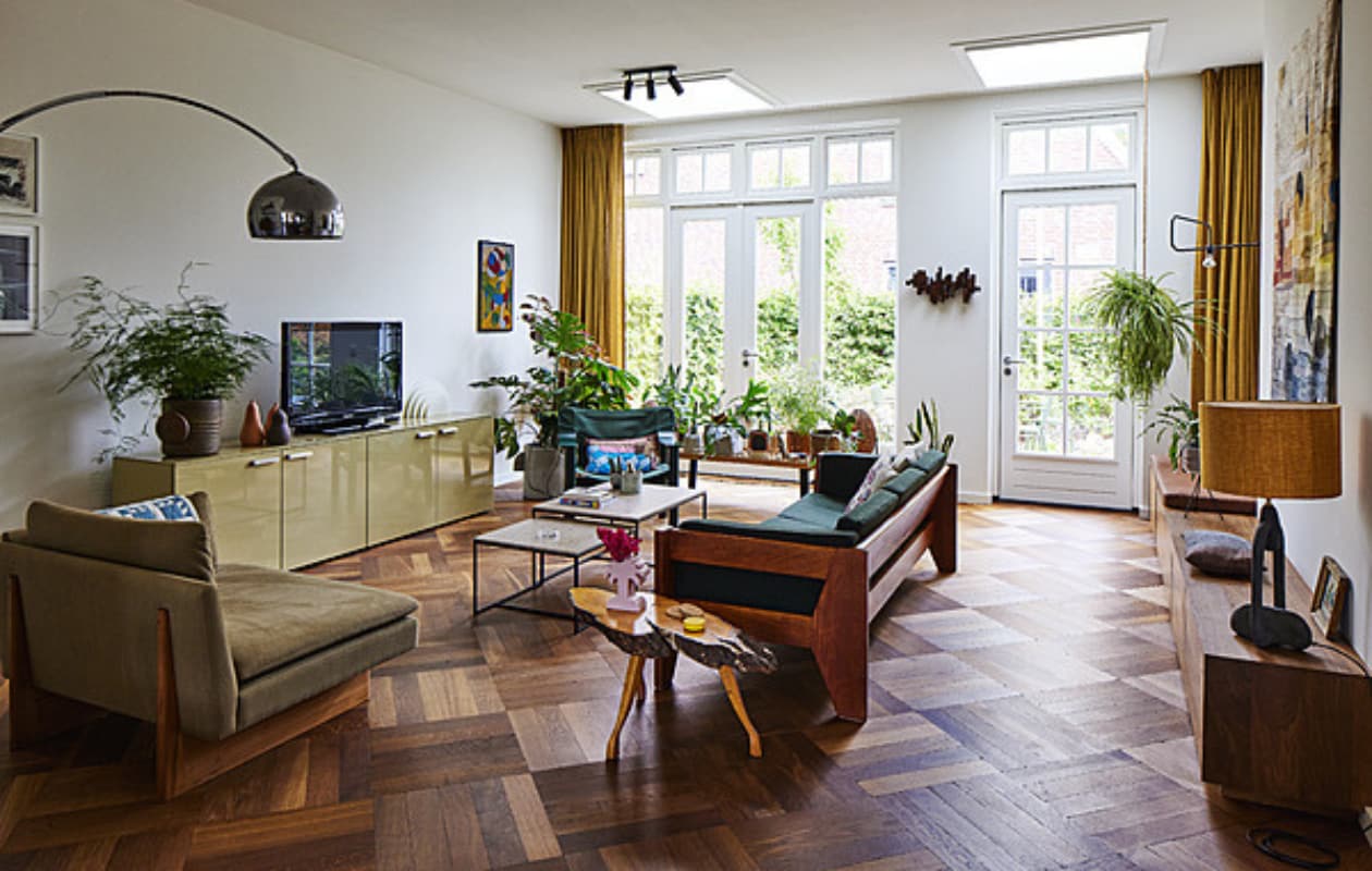 Loveseat Sofa, muurlamp, schemerlamp, wandkleed en muurbank X+L. Groene bank, peren, bijzettafel boom, klein schilderij vintage. Kussens zelfgemaakt, palmboomvaas Stüssy, salontafels Schriever Interieurbouw, dressoir Cappellini, vintage plantenpot Mobach Keramiek, witte lamp Raak, vilten kunstwerk Marktplaats, groene fauteuil Hay, kussen A.p.c., houten bank Nelson Platform Bench. Diverse potten Wildernis, vintage en Serax. Wandsculptuur Ming Stylemeister, spotjes Sofisticato van Koen Van Guijze van Serax. Overig onbekend. vtwonen 11-2023 | styling Mariella Kallenberg | fotografie René Mesman