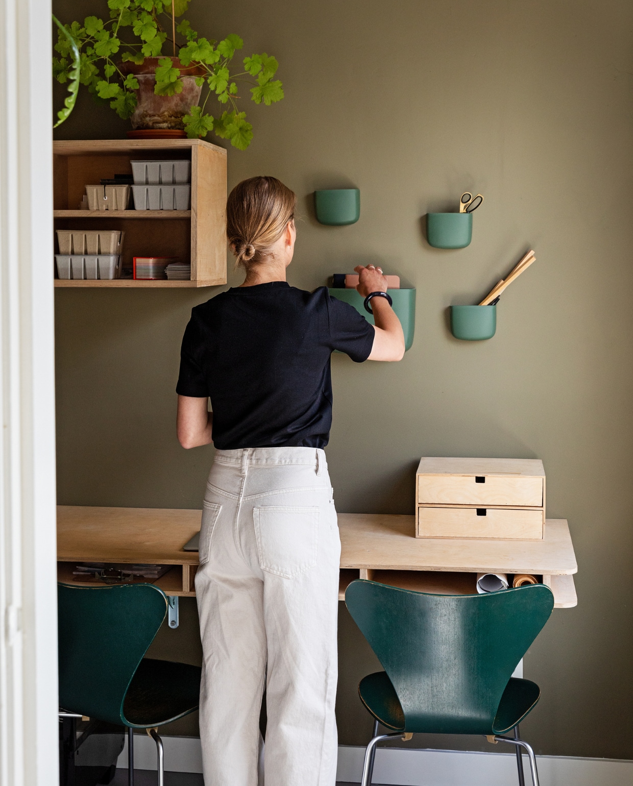 Muurkleur RAL 7002. Bureau en wandkast zelfgemaakt. Vlinderstoelen van Fritz Hansen via VintageMarket. Planten en opbergdozen Nørd Conceptstore. Wandbakjes Normann Copenhagen. vtwonen 10-2022 | Styling Ilona Jongepier | Fotografie Dana van Leeuwen