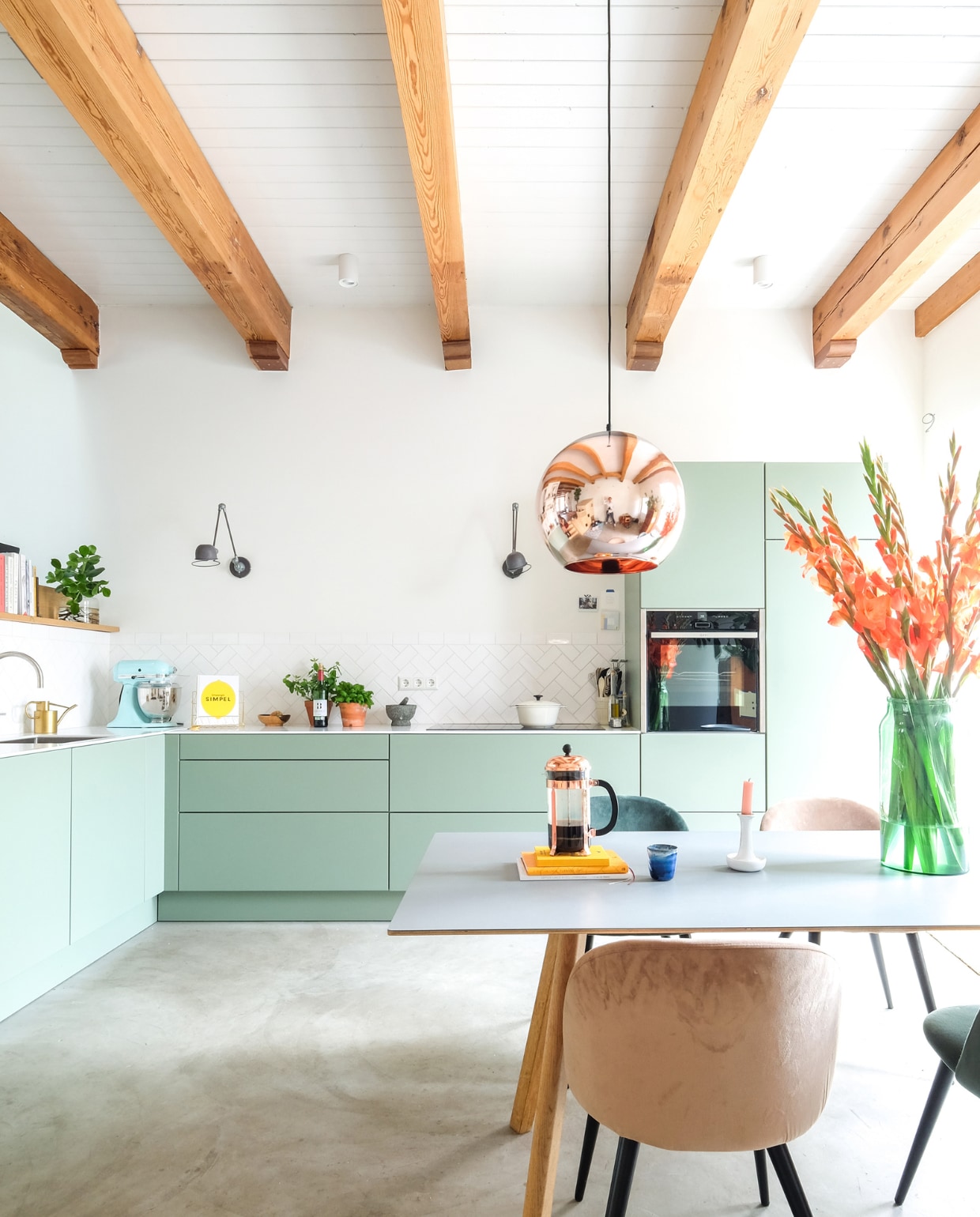 Keuken Next125, kleur Sage. Tafel Hay. Hanglamp Tom Dixon. Herkomst stoelen onbekend. Vaas Bloemetje Op Tafel. Kandelaar Hay. Cafetière Bodum. Pan Ikea. Wandlampen Lucide. vtwonen 03-2021 | productie Coco features | styling Gerlise van putten | fotografie Sabine Burkunk