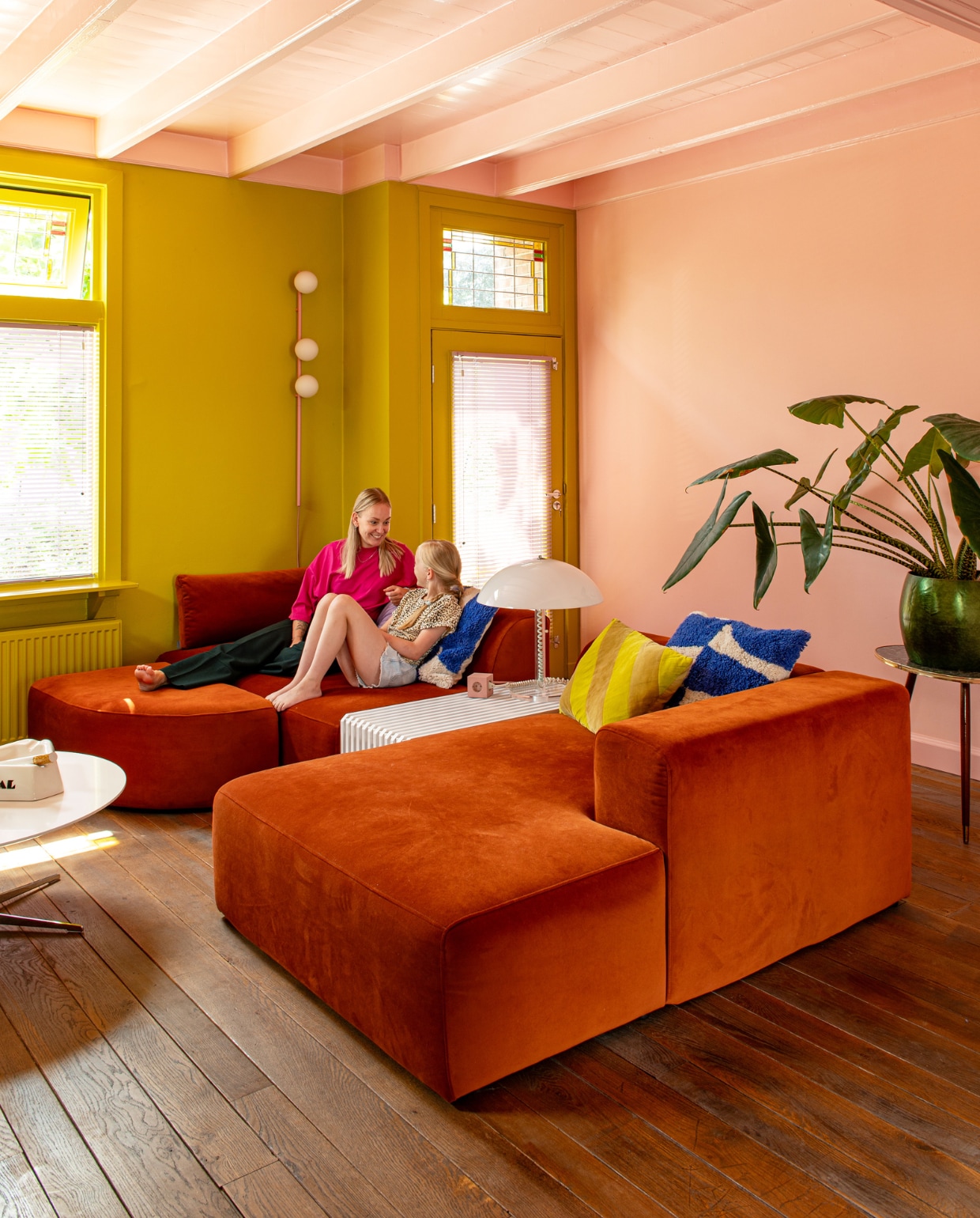 Bank 4x6 Sofa. Bijzettafel en geel kussen HKliving. Lamp Harco Loor, wandlamp Houseof, blauw-witte kussens H&M, tafel uit Deense kringloop, asbak Seletti voor Diesel, plantentafel kringloop, pot lokale winkel. Roze verf wand en plafond Zalm en   geelgroene muurverf Wildernis van Gamma. vtwonen 11-2023 | productie De Binnenkijkers | styling Jeske Weel | fotografie Caroline Coehorst