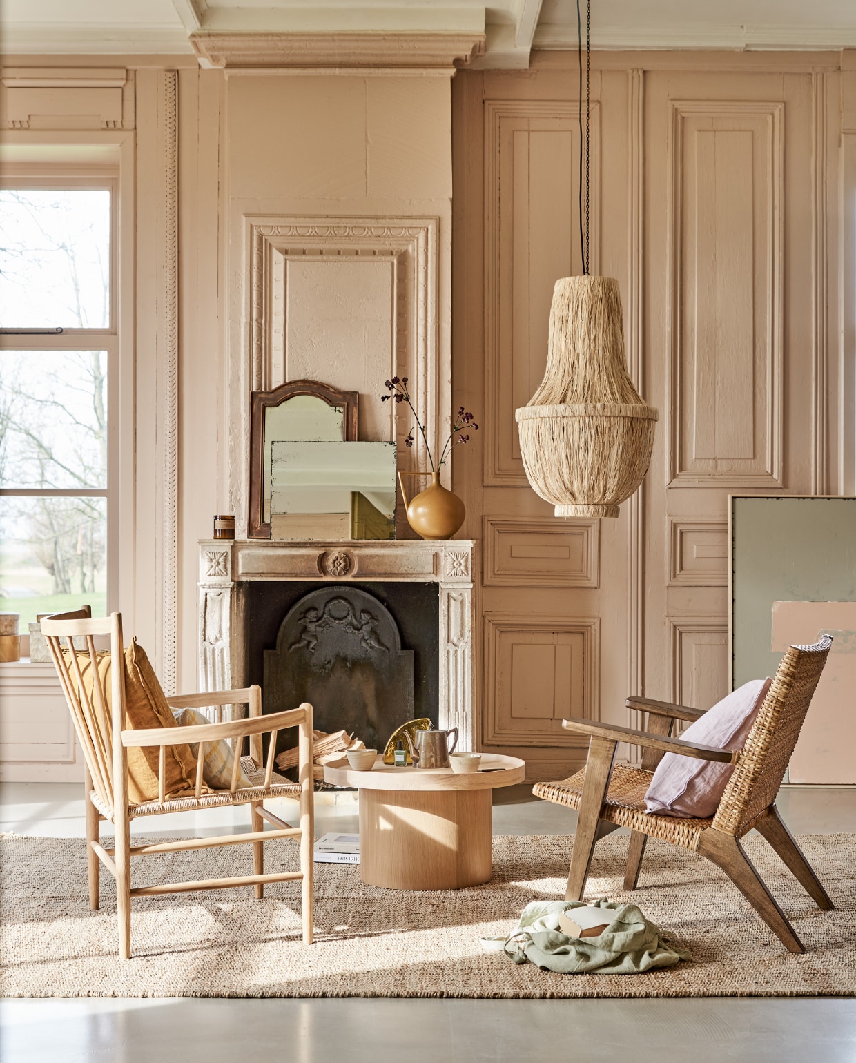 Fauteuil links FD Møbler J82 Jørgen Baekmark Lounge Chair vanaf € 1080,-, linnen tas € 37,90, geruit kussen€ 39,90, geurkaars € 27,90, mokken op tafel per stuk € 9,90 (letoile.store). Fauteuil rechts € 595,- vloerkleed, 200x300 cm € 349,-, kunstwerk Abstract 100x120 cm € 549,-, rechthoekige spiegel antieklook € 59,95, vaas in mosterdkleur € 47,95, glazen artwork op tafel € 59,95 (hkliving.nl). Zacht lila kussen van Bungalow € 47,-, okergeel kussen € 47,-, papieren dozen set van 2 € 36,- (scandicliving.nl). Oude spiegel met houten rand € 65,-(com-anders.nl). Salontafel Plateau van Bolia, 34,3x61 cm (hxØ) € 579,- (vtwonen.be). Kroonluchter van gedroogde bananenbladeren € 599,- (rivieramaison.com). Kleur op de wanden vergelijkbaar met Setting Plaster No.231 van Farrow &amp; Ball. vtwonen 05-2021 | styling Marlies Does | fotografie Bart Brussee