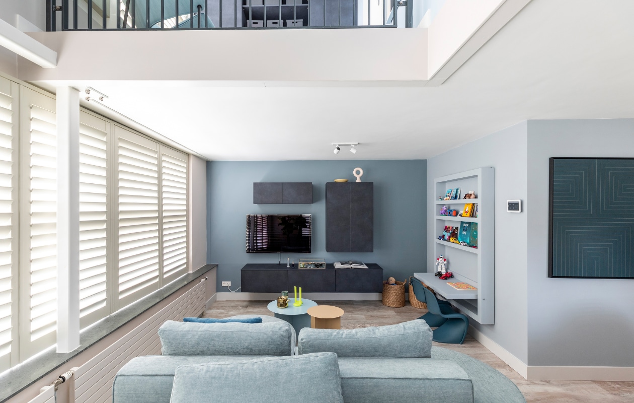 Flexa Creations muurverf bij wand met shutters Sandy Steps, achter tv Denim Drift, muur kinderhoek en kinderhoek Blissful Blue, plafond Denim Drift, muur entresol Kleur van het Jaar 2022 Bright Skies (flexa.nl). Shutters kleur Cream Grey, prijs op aanvraag (jasnoshutters.nl). Zwevend dressoir en kasten in kleur Lime Midnight, prijs op aanvraag (woninginrichting-aanhuis.nl). Elementenbank Loki van Studio Mik € 4683,-, vloerlamp Bolt van Tonone € 450,-, vloerkleed Haven van Bic Carpets op maat gemaakt, prijs op aanvraag (eijerkamp.nl). Blauwe bijzettafel van HKliving € 249,-, crèmekleurige bijzettafel van HKliving € 149,-, donkerblauw kussen Dot van Hay € 85,-, kopjes van HKliving € 8,99, theepot Bold &amp; Basic van HKliving € 49,95, junior kinderstoelen Panton van Vitra € 185,-, aan plafond begane grond dimlamp Runner 2 Spot van Philips € 89,99 (vtwonen.nl). Gele kaars Twist van Lex Pott € 29,95 (groenenakker.nl). Showcase box, per 2 € 206,- (polspotten.nl). Op dressoir opbergdoos vitrine van vtwonen € 44,95, kandelaars Lavender Tube van Hay € 18,- en Midnight Blue Tube van Hay € 15,- (vtwonen.nl). Papieren beestjes vanaf € 11,75 (assemblishop.com). Ornament Circle on Base van HKliving € 40,-, geel bord van HKliving € 12,50 (eijerkamp.nl). DIY-kinderspeeltafel met kast, prijs op aanvraag (remmers-design.nl). Manden Insvep, per stuk € 29,99 (ikea.nl). Op entresol studeerplek met kastensysteem in kleur Lime Midnight, prijs op aanvraag (woninginrichting-aanhuis.nl). Kunstwerken in deze uitvoering Vormen #10 van Adriano Oliveira € 151,-, Vormen #05 van Adriano Oliveira € 151,- (werkaandemuur.nl). Tafellamp Bolt van Tonone € 345,-, fauteuil Glider van Artifort € 2009,- (eijerkamp.nl). Opbergdozen Tjena, per stuk € 2,99 (ikea.nl). Overig privébezit. vtwonen weer verliefd op je huis seizoen 15 aflevering 10 | styling Marianne Luning | fotografie Margriet Hoekstra