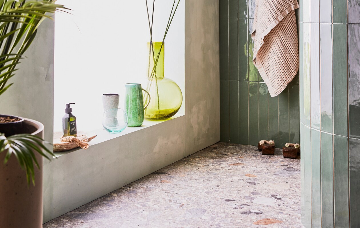 Donkere wandtegel Marrakesh kleur Army Green glans 6,5x40 cm, lichte wandtegel Marrakesh kleur Seagreen, glans 6,5x40 cm, vloertegel Composite kleur Multicolor 120x120 cm en badlakens van Marc O'Polo vtwonen.nl, planten pot nordal.eu, groene kan bungalow.dk, handzeep Meraki hm.com, grote groene glazen vaas hkliving.nl. Overig privébezit. vtwonen 08-2021 | styling Cleo Scheulderman | fotografie Jeroen van der Spek