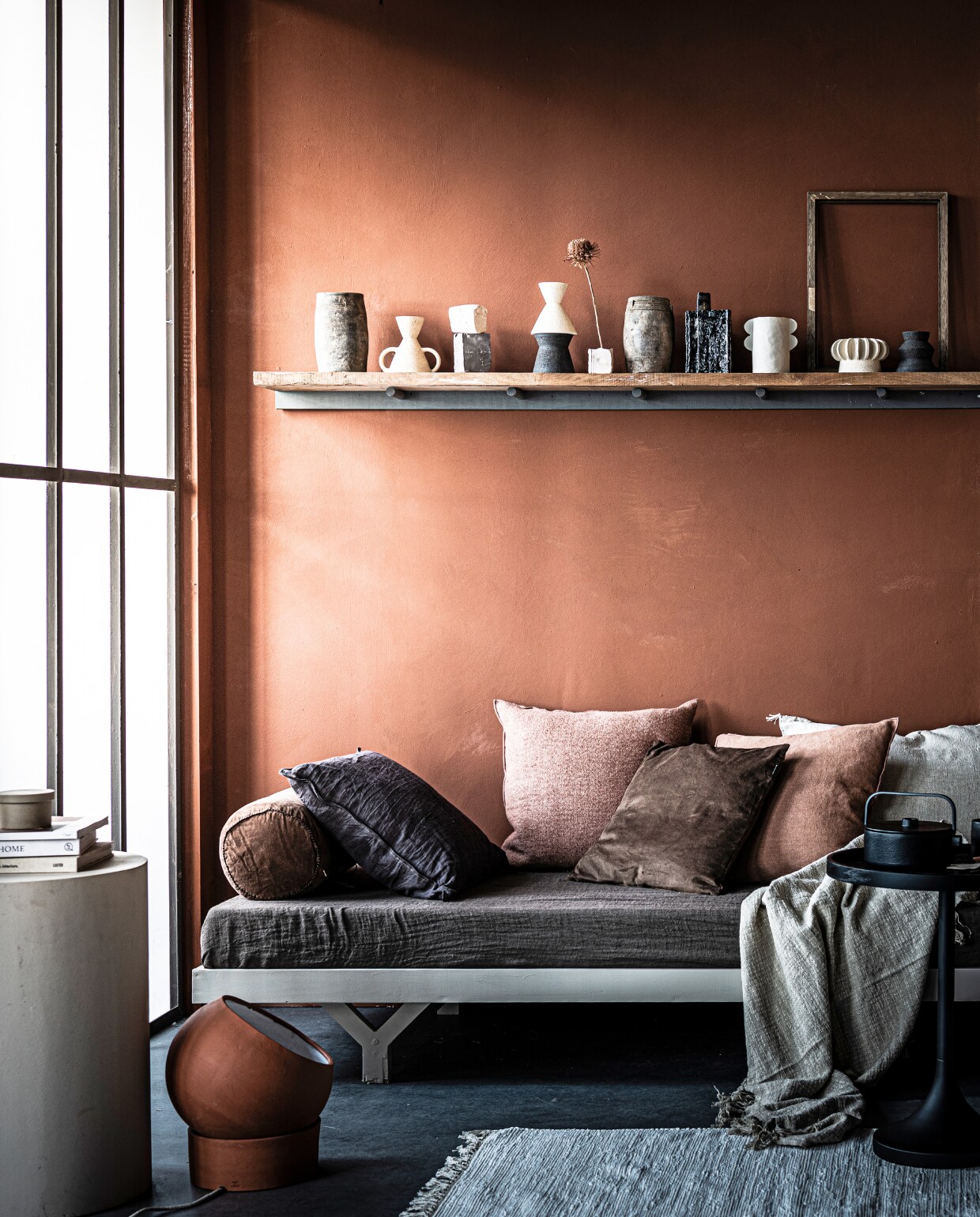 Muurkleur Fresco in Terracotta (pure-original.nl). Loungebed op maat gemaakt € 375,- (com-anders.nl). Op het loungebed: plaid Vice Versa in Terre van Maison de Vacances € 195,-, kussen Vice Versa Toile Nomade van Maison de Vacances € 146,-, kussen Vice Versa stone washed linnen van Maison de Vacances € 133,-, kussen off white Sabra Oblong XL € 113,- (couleurlocale.eu). Rond velvet kussen Bolster van Madam Stoltz € 39,25 (deens.nl). Bruin kussen van vtwonen collectie € 33,80, bruin velvet kussen € 30,95, plaid € 27,99, bijzettafel Jason van Zuiver € 99,95, lamp van klei van Serax € 124,95 (vtwonen.nl). Betonnen bijzettafel privébezit. Op de plank: hoge potten € 42,- (couleurlocale.eu), kleine vazen in wit, bruin en zwart uit de Earth series vanaf € 37,50, witte vaas met 4 oren Eyra € 50,- (studio-yen.com). Vaas abstracte vorm van Serax € 35,05, theepot Collage van Serax € 89,- (vtwonen.be). Ronde zandkleurige doos € 19,- (fermliving.com). Vloerkleed € 19,99 (hm.com). Wandplank privébezit. vtwone 03-2021 | styling Marlies Does | fotografie Sjoerd Eickmans