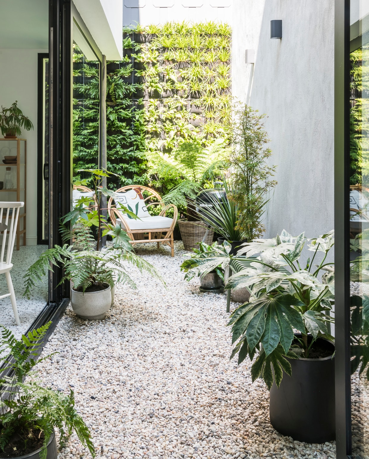 Van de binnenplaats maakte het stel een groene oase met eenmuurtuin en plantenbakken. De rotan fauteuil is van Tine K Home,de hangstoel van Casa. De zandkleurige kiezels sluiten mooi aanop de terrazzovloer van de keuken. vtwonen 13-2019 | styling &amp; fotografie Jonah Samyn