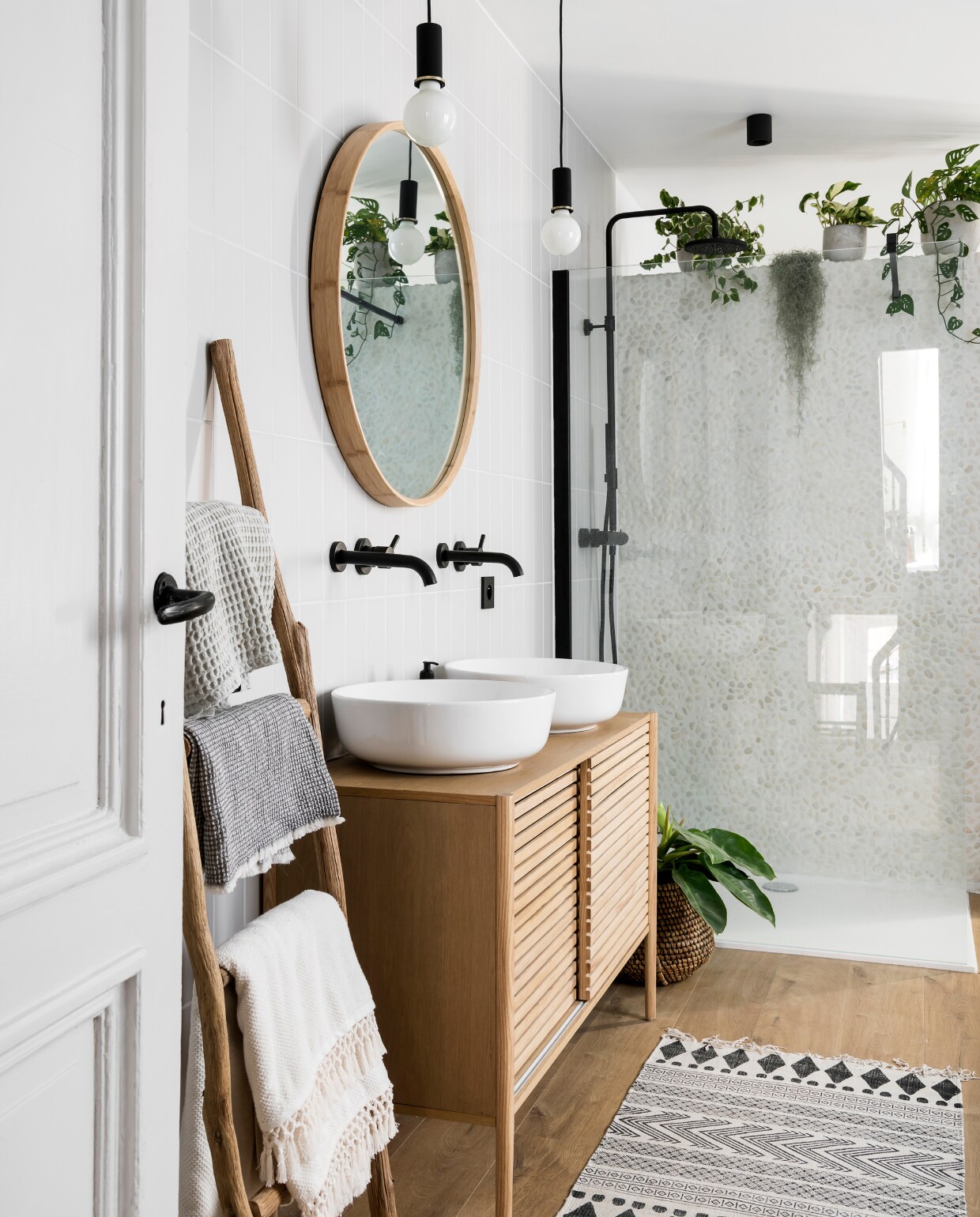Blikvanger is de muur met kiezelstenen die bewust niet tot aan het plafond komt zodat er plaats overblijft voor heel veel planten. Badkamerkamermeubel gemaakt van een dressoir van Maisons du Monde. Ronde spiegel van Hübsch, sierladder van HKliving. Daaraan hangen handdoeken van H&amp;M en Ferm Living. vtwonen 13-2019 | styling &amp; fotografie Jonah Samyn