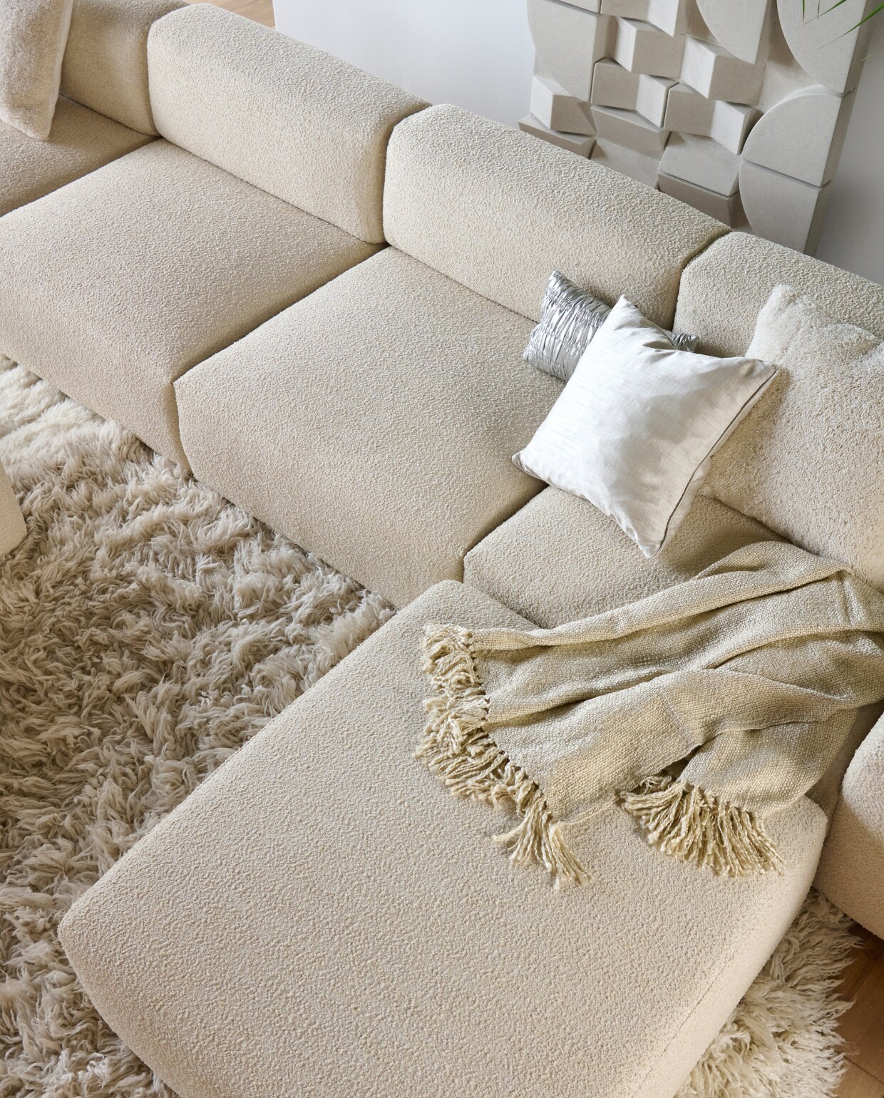 Elementenbank Cubi Spacious en poef Large, allebei van Basta in Linen Melé  (basta.co). Hoogpolig vloerkleed Fluffy, wol en katoen, 250 cm (Ø) (hkliving.nl). Wandpaneel Montañas, 175x100 cm (lanena-home.com). Acryl plaid Solid van Malagoon in Ivory (vtwonen.nl/shop). Wollen kussen Tufted Solid (malagoon.com). Zilveren katoenen kussen New Age van HKliving (loods5.nl). Zijdeglanzend kussen (nordal.com). vtwonen 2023-11 | Styling Marianne Luning | Fotografie Sjoerd Eickmans