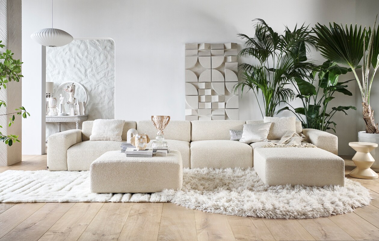 Elementenbank Cubi Spacious € 4420,- en poef Large € 610,-, allebei van Basta in Linen Melé  (basta.co). Houten parket XL in geolied eiken white wash van vtwonen, per m2 € 94,95, muurverf krijtlook Snow White van vtwonen, per 2,5 liter € 46,99 (karwei.nl). Hoogpolig vloerkleed Fluffy, wol en katoen, 250 cm (Ø) € 1575,- (hkliving.nl). Wollen vloerkleed van Brinker Carpets, hoog- en laagpolig, 200x290 cm € 1250,- (eijerkamp.nl). Wandpaneel Montañas, 175x100 cm € 1249,- (lanena-home.com). Polyester bijzettafel Zig Zag van Polspotten € 345,-, hanglamp Nelson Saucer Bubble van Hay € 695,-, acryl plaid Solid van Malagoon in Ivory € 49,95, aardewerken vaas Moire van Ferm Living € 139,- (vtwonen.be/shop). Wollen kussen Tufted Solid € 59,95 (malagoon.com). Zilveren katoenen kussen New Age van HKliving, € 49,95, porseleinen gebouwen van Joost Gijzel, per stuk € 79,- (loods5.nl). Zijdeglanzend kussen € 50,-, aardewerken plantenpot € 225,- (nordal.com). Marmeren boekensteun Ferro van Nordal € 68,- (deens.nl). Tweedehands wandtafel € 100,-(delokatie.nl), geverfd in hoogglans lak White Wood nr. 201 van Lab Paint, 500 ml € 47,- (vestingh.nl). Kunstobjecten, aardewerk en gerecyclede materialen, vanaf € 150,- (vazenvanjanssen.nl). Gipsen cirkel € 85,-, venusbeeld € 59,90 (het-schippertje.nl). Overig privébezit. vtwonen 2023-11 | styling Marianne Luning | fotografie Sjoerd Eickmans