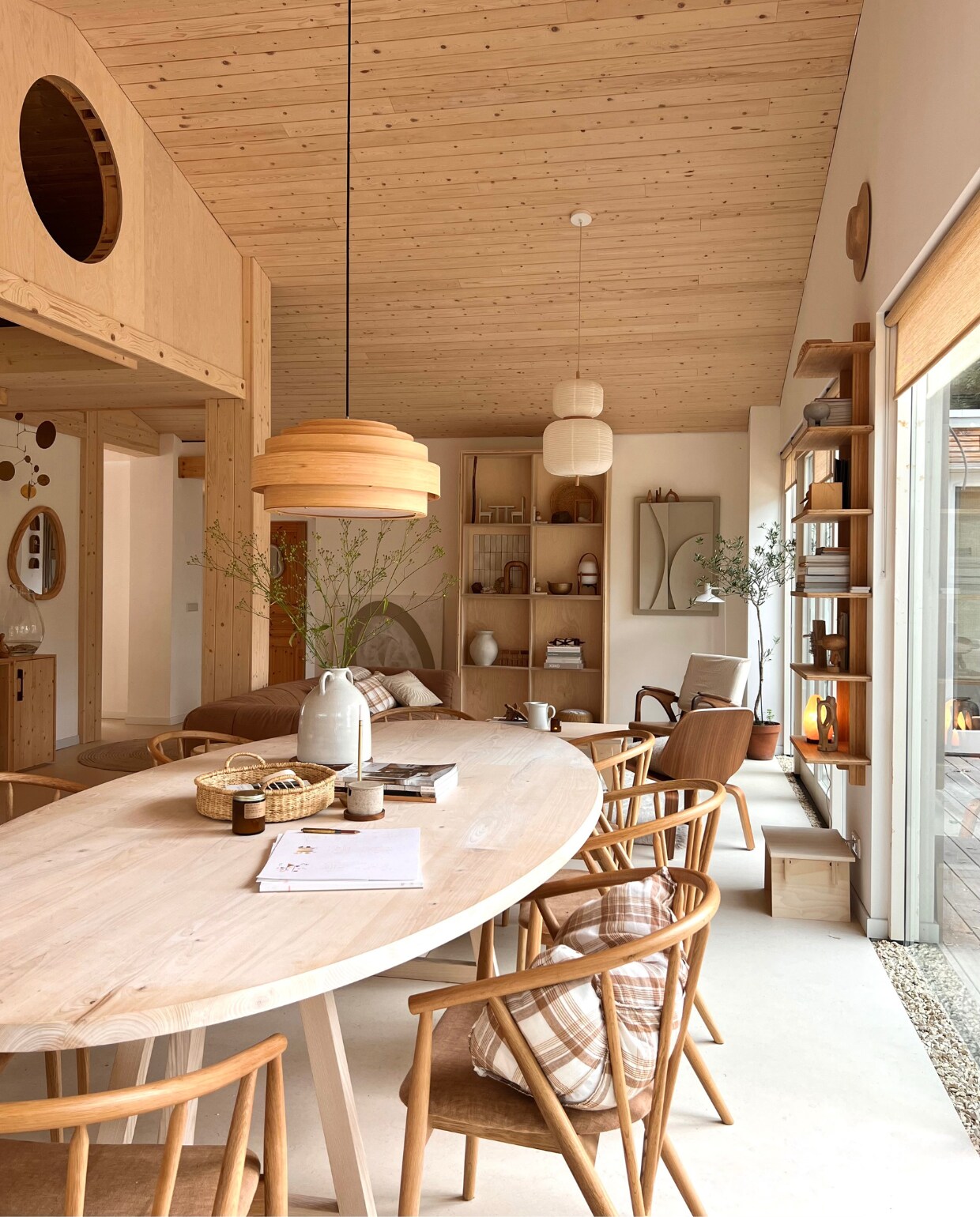 Houten eettafel SlowWood, aardewerken vaas Tine K Home, gevlochten schaal Dille &amp; Kamille, houten eetkamerstoelen en fauteuils Marktplaats, bamboe hanglamp Thin Wood van Ay Illuminate van FunDesign, rijstpapieren hanglamp Misaki van Westwing, bank Arflex, open boekenkast zelfgemaakt, schilderijen links Viola Luhrman, rechts Art-in-return, houten wandplanken Ask &amp; Eng, houten kruk eigen design Woodchuck. vtwonen 2023-11 | Productie Rolien van der Leeuw | Fotografie Tinta Luhrman