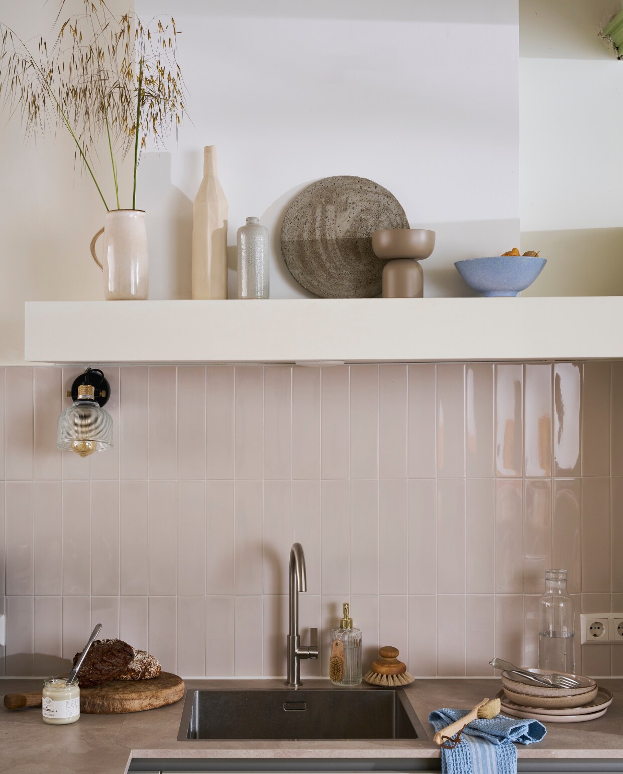Composiet spoelbak met goudkleurige kraan, prijs op aanvraag.  Wandtegels Shapes in Vapor van vtwonen per m2 € 59,-. M.m.v. hm.com (kom, borden, theedoek, schaal op voet, kan, serviesgoed, bord), bolia.com (karaf, vaas) vtwonen catalogus 2023