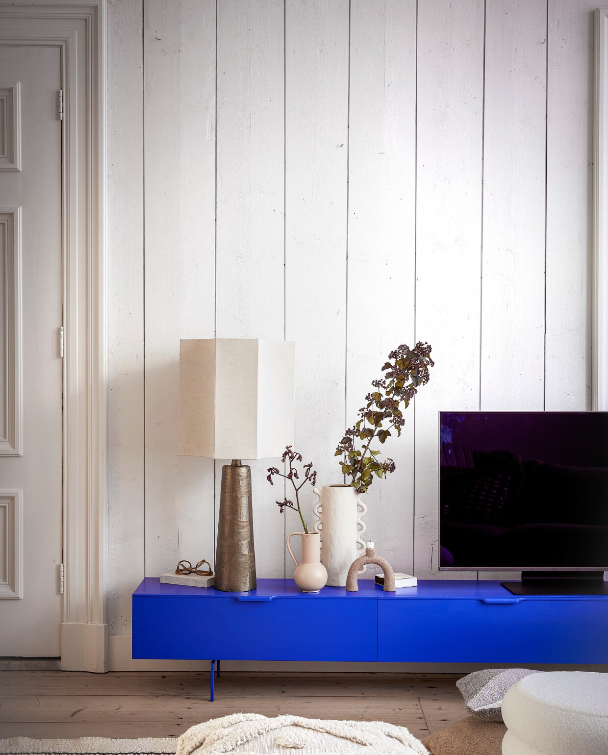 Sungkaihouten, kobaltblauw tv-meubel van HKliving, 250x30x36 cm (lxbxh) € 1195,- (vtwonen.nl/shop). Linnen hexagon lampenkap € 69,95, lampenvoet € 79,95, poef Tufted € 79,95, naturel kussen Florine € 39,95 (loods5.nl). Kandelaar € 7,- (kringloopwinkel). Witte keramieken vaas met Ruffle € 39,99, notitieboek € 17,99 (sissy-boy.com). Neo QLED 4K televisie, 43 inch, prijs op aanvraag (samsung.com). Katoenen vloerkleed, 150x240 cm € 299,- (hkliving.nl). Polyester poef Prato € 45,-, kussen Turijn bovenop ander kussen € 12,50, kleine vaas € 9,50 (kwantum.nl). Bril (aceandtate.nl). vtwonen 12-2023 | styling Kim Timmerman | fotografie Peggy Janssen
