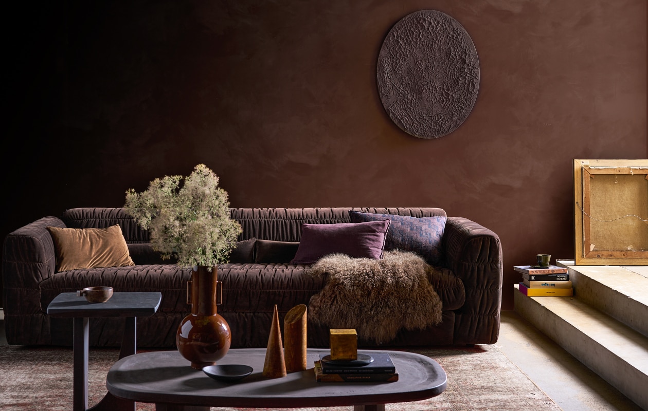 Muurverf kalkverf Aubergine 46, per 2,5 liter € 146,90 (lauthentique.nl). Fluwelen 4-zitsbank Club Couch in Espresso, 274x108x72 cm (bxdxh) € 2795,- (hkliving.com). Ovale houten salontafel Fille met betonlook finish, 120x75x35 cm (lxbxh) vanaf € 1745,-, eikenhouten bijzettafel Kurv, gekleurd met gepigmenteerde olie, 45x45x50 cm (bxdxh) vanaf € 625,- (boxworx.nl). Bruine keramieken vaas van HKliving in Espresso € 73,99, kussen met diagonale strepen van HKliving, 60x40 cm (bxh) € 59,- (vtwonen.be/shop). Zwarte metalen schaal € 17,-, groene beker Grawa € 9,09 (nordal.com). Schapenvacht € 99,-, fluwelen kussen links, 50x70 cm € 34,95 (iblaursen.nl). Houten geometrische objecten, prijs op aanvraag (graublau.nl). Zelfgemaakt canvas muurobject van schilderdoek, 40x50 cm € 36,99 (amazon.nl). Vintage vloerkleed, soortgelijk (rozenkelim.nl). Auberginekleurige fluwelen kussenhoes Astrid van Claudi, 60x40 cm € 69,- (wilhelminadesigns.com). Plafondkleur onbekend, overig privébezit. vtwonen 12-2023 | styling Cleo Scheulderman | fotografie Jeroen van der Spek