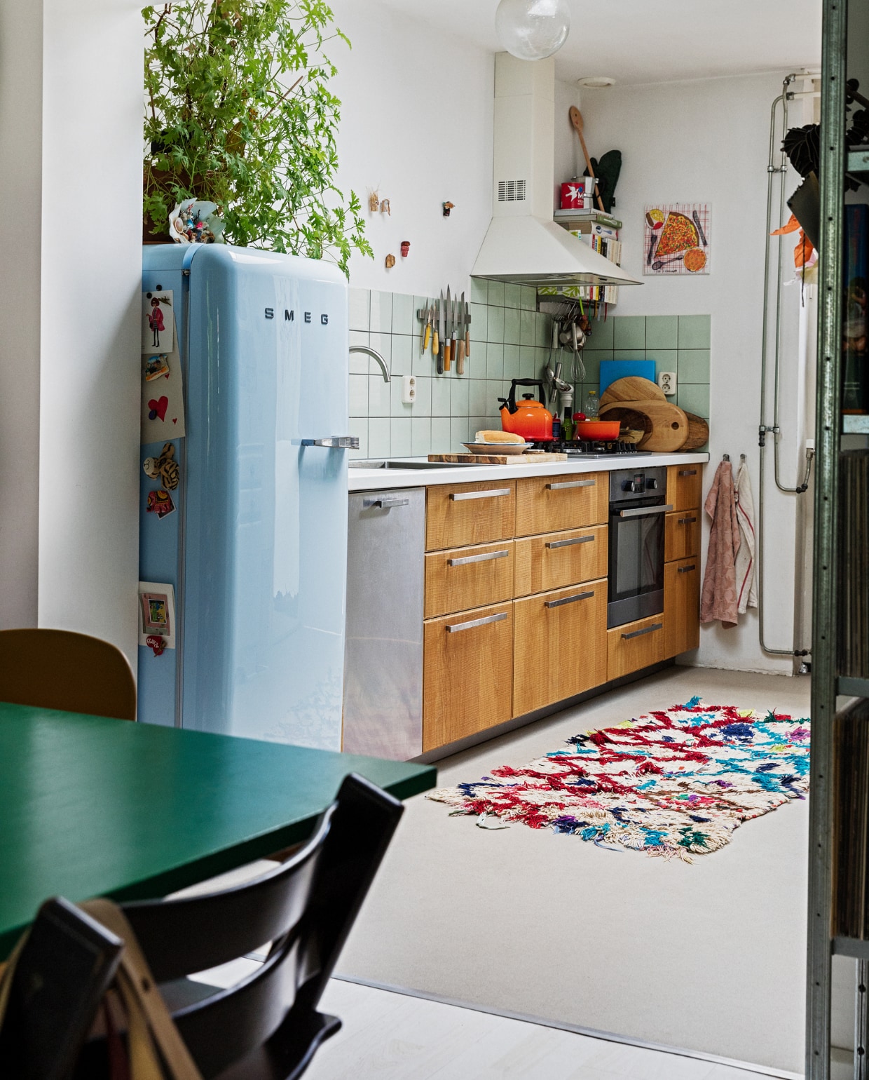 Koelkast Smeg. Geraniumplant zelf gestekt. Kitsch schelp op koelkast souvenir uit Griekenland. Magneet-souvenirs meegenomen van verschillende reizen. Fluitketel en pan Le Creuset. Messen Suncraft, Opinel, Dille &amp; Kamille, Pallarès Solsona. Snijplanken Hay, Ikea, Serax. Soeplepel Brabantia. Rvs keukengerei Dille &amp; Kamille. Schaaltje van een pottenbakkersmarkt. Afzuigkap en oven Ikea. Ovenhandschoen Kook. Pollepel Kookhuis aan de Maes. Handdoeken Sissy-Boy. Tapijt The Souks. Pizza-schilderij Oskar. Ronde plafondlamp lampenwinkel.nl. Overig privébezit. vtwonen 13-2021 | styling Ilona Jongepier | fotografie Dana van Leeuwen