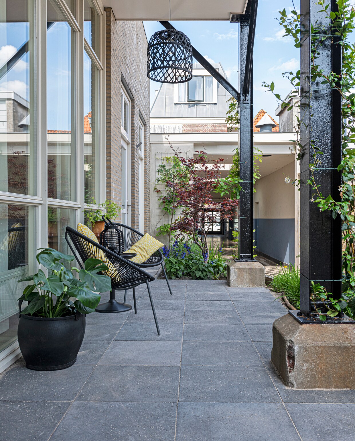 Het terras voor het huis. Stoelen Karwei, kussens Ikea, hanglamp Kwantum, rubberen mand Household Hardware. Tegels Koornneef De Lier. vtwonen special binnenkijken 12-2020 | styling Sharon Roest | fotografie Caroline Martinot