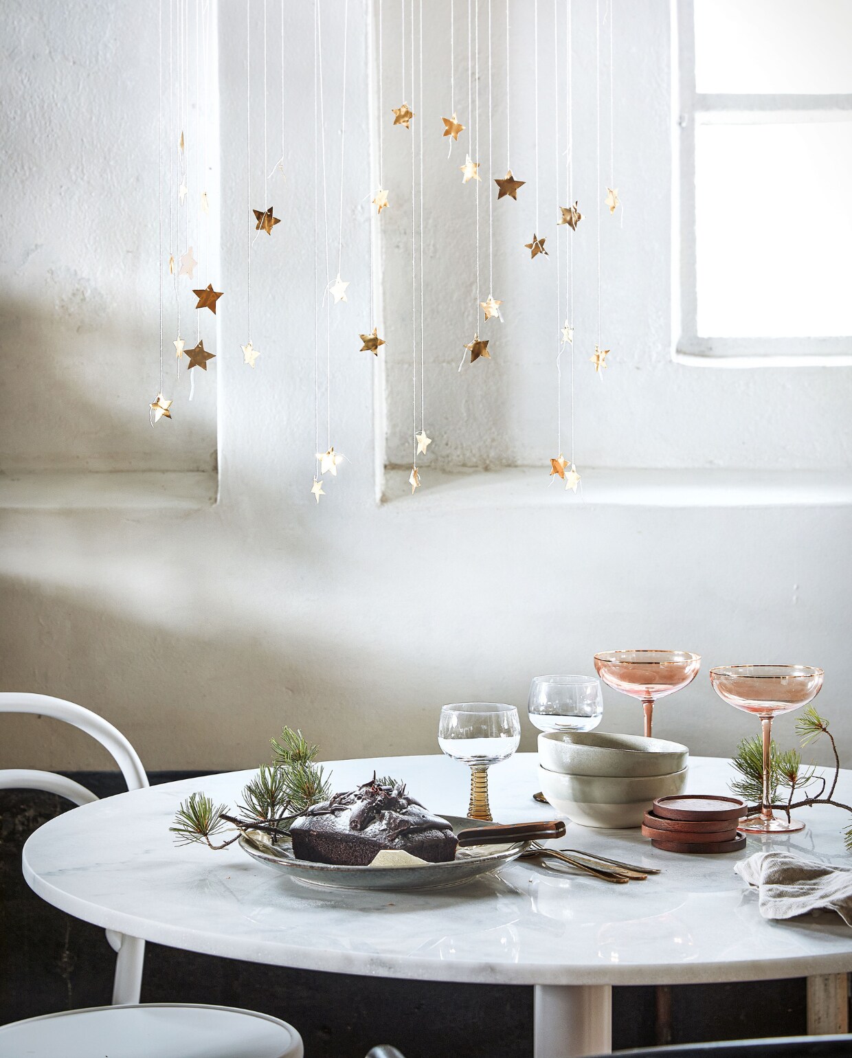 Eettafel Cadiz van Vestbjerg(vtwonen.nl). Stoel met armleuning en webbing zitting, zwarte stoel zonder armleuning, witte stoel, linnen servet (dille-kamille.nl). Glazen met groene voet (hkliving.nl). Roze glazen van Nordal, groen bord van Madam Stoltz (deens.nl). Overig privébezit. vtwonen 12-2021 | styling Marlies Does | fotografie Peggy Janssen