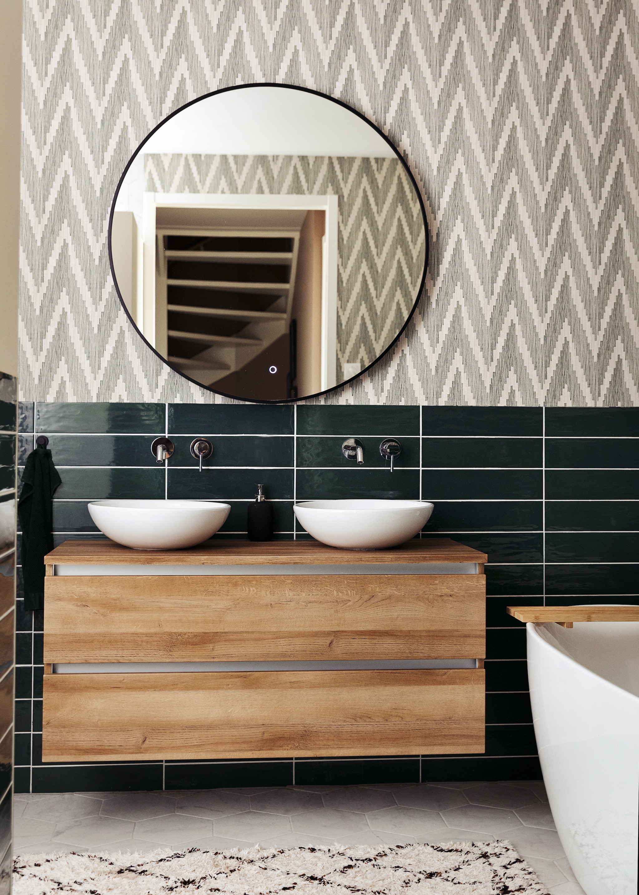 Badkamerkast Unihopper. Wastafelkommen Solid Surface. Kranen en vrijstaand bad ADW. Spiegel Best Design. Tegels Sartoria. Behang BN Walls. Kleed H&amp;M Home. vtwonen 10- 2021 | styling Ilona Jongepier | fotografie Dana van Leeuwen