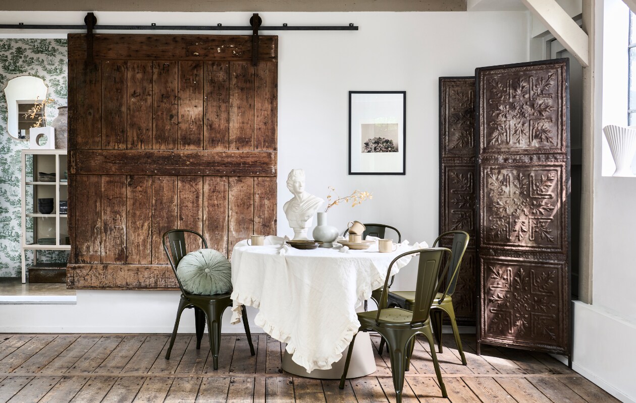 Mdf eettafel Jorre van Woood in Militair Brown, 120x76 cm (Øxh), ijzeren stoel Afternoon van vtwonen, porseleinen vaas Tank van BePureHome, velvet kussen Halo van BePureHome (basiclabel.nl). Metalen kamerscherm van oude plafonddecoratie, 188x2x194 cm (lxbxh) (hetkabinet.nl). Vintage borstbeeld (fortuneflea.com). Bekers en borden uit serviesset Yard Picnic in kleur Cashmere van Ferm Living, 8-delig, metalen borden uit picknickset Yard Picnic van Ferm Living in Cashmere en Olive, 8-delig (vtwonen.be/shop). Overig privébezit. vtwonen 11-2023 | styling Marlies Does | fotografie Sjoerd Eickmans
