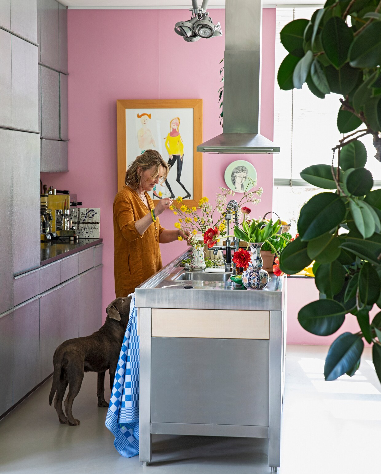 Karen aan het kookeiland van rvs en eikenhout. Apparatuur Smeg. Op maat gemaakte keuken met fronten van zink. Lamp Modular. Kunst Vanessa Beecroft. Wandbord meegenomen uit Australië. Roze muurverf Histor S0540-R30B. Overig herkomst onbekend. vtwonen 07-2021 | styling Ilona Jongepier | fotografie Dana van Leeuwen