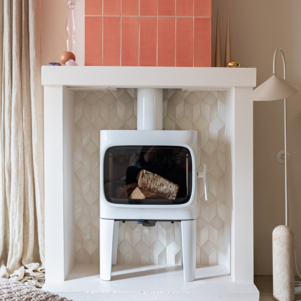 Houtkachel Jotul F305. Tegels 1030 cm kleur Flamingo Baby en witte tegels Constellation kleur Eggshell White via Quintalisque. Kussen Sukha. Lamp en kiezel Ferm Living. Glazen kandelaar herkomst onbekend. Kaarsen Ester &amp; Erik. vtwonen 02-2022 | styling Ilona Jongepier | fotografie Dana van Leeuwen