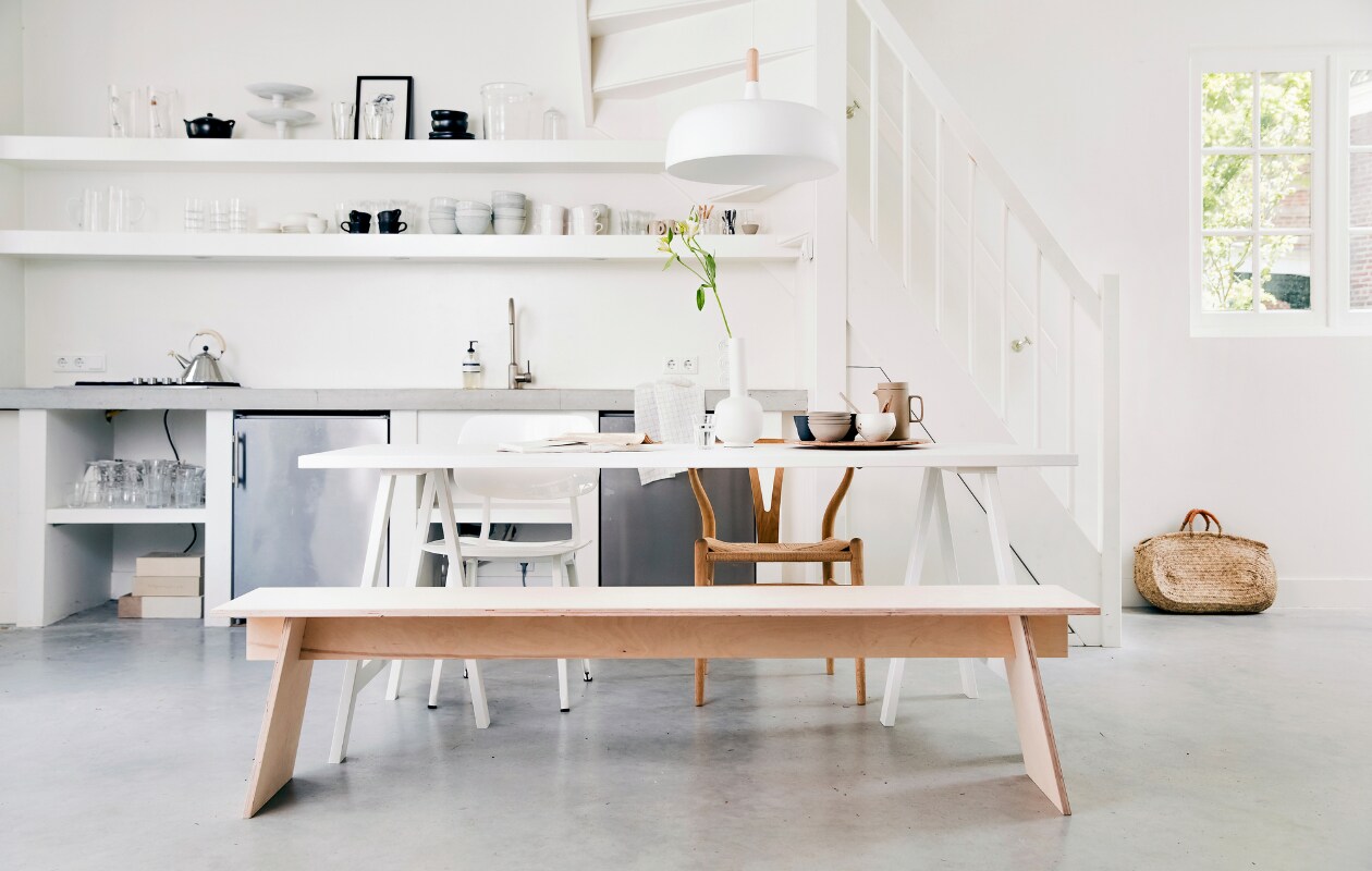 Bankje DIY, Tafel onderstel Brace in wit geschilderd essenhout van vtwonen, tafelblad Panel in wit geschilderd essenhout van vtwonen 190x80 cm, hanglamp Northern Acorn van Nordic Nest, witte vaas Muses Clio van Ferm Living, houten vogel S, tafellamp Milk van &amp;tradition, kandelaar Balance van Ferm Living (vtwonen.be). Houten stoel Wishbone van Carl Hansen, witte stoel Revolt van Ahrend (misterdesign.nl). Porseleinen theepot van Hasami (thefinestore.com). Theedoek (hm.com). Bord met reliëfdruk plant (studioharmenelke.nl). Print van Loulou Avenue (loods5.nl). Overig privébezit. vtwonen 07-2019 | styling Kim van Rossenberg | fotografie Ernie Enkelaar