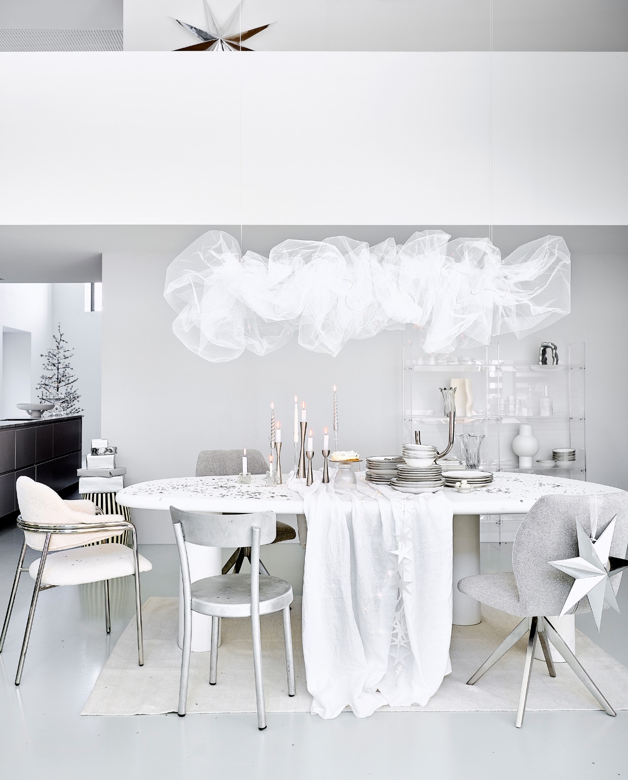 Eetkamertafel Bloomstone, mdf met lichte ecoplaster finish, 230x117x78 cm (bxdxh) € 1530,- (richmondinteriors.nl). Acryl vakkenkast 137x27,8x160 cm (bxdxh) € 1195,-, matwitte vaas € 49,95 (hkliving.com). Witte eetkamerstoel Albert Chair, teddystof en staal, 56x59x84 cm (bxdxh) € 605,30, verchroomde kandelaar € 87,25, zwart-witte bijzettafel, mdf en  mangohout, 41x41x48 cm € 530,30, glazen taartplateaus € 41,67, glazen vaas € 106,06 (nordal.com). Aluminium eetkamerstoel € 680,- (framacph.com). Grijze eetkamerstoel, polyester en staal € 229,- (jesperhome.com). Glazen ster, vierkante kandelaar, per stuk € 22,50 (alltheluckintheworld.nl). Servies van vtwonen vanaf € 7,95, metalen kandelaars, 16 cm € 16,95, 20 cm € 19,95 en 25,5 cm € 24,95, zilveren ster van papier, 110 cm € 29,95, ster 48 cm € 14,95, bestek Montreux van Sola, 50-delig € 115,99, schaal Earth van Serax, papier en pulp € 146,-, glazen etagère Damo van Ferm Living € 239,- (vtwonen.nl/shop). In kast: aluminium ornament € 135,-, geribbelde karaf € 39,-, geribbelde glazen van Ferm Living, set van 4 € 39,-, geribbeld glazen schaaltje van Ferm Living, set van 4 € 59,-, witte vaas Moire van Ferm Living € 139,-, glazen vaas Holo van Ferm Living € 71,99 (vtwonen.nl/shop). Linnen tafelkleed € 69,99, vloerkleed, 160x230 cm € 199,-, glazen kandelaars vanaf € 9,99 (zarahome.com). Gedraaide kaarsen, set van 6 € 15,95 (kunstindustrien.dk). Witte kaarsen € 1,- (hema.nl). Aardewerken schaal € 5,99 (hm.com). Kerstboom Alfi Tree van Sirius, 150 ledlampjes, 180 cm (h) € 275,-, papieren sterrenslinger van Räder € 16,95, lichtsnoer bloemen € 32,50 (two-gether.nl). Zilveren confetti € 9,20 (partywinkel.nl). Inpakpapier € 2,95 (vliegerpapier.nl). vtwonen bijlage kerst 2023 | styling Kim van Rossenberg | fotografie Louis lemaire