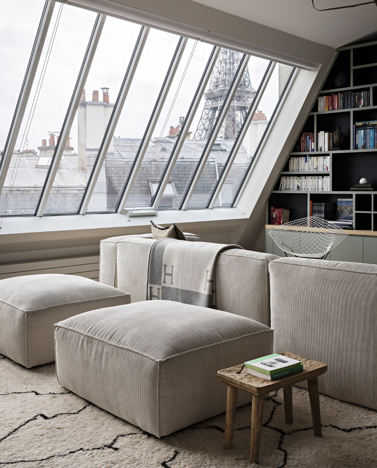 Bank La Redoute. Vloerkleed en plaid Mustapha Blaoui. Salontafel &amp;Tradition. Boekenkast en ramen op maat gemaakt. Hanglamp Ay Illuminate, stoel van Harry Bertoia voor Knoll. Poefs vlooienmarkt. Overig onbekend. vtwonen 12-2023 | productie AC Scoffoni | styling Marie-Maud Levron | fotografie Yann Deret | tekstbewerking Merel van der Lande