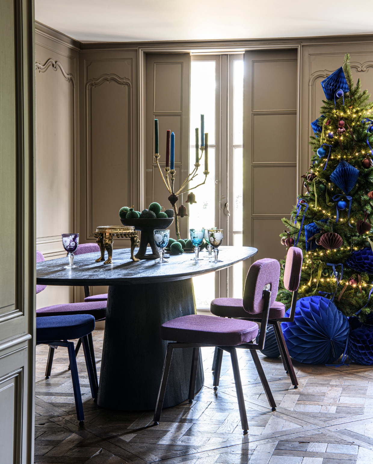 Bruine mangohouten eettafel Aron, 300x110x76 cm (bxdxh) € 1499,- (eleonora.nl). Eetkamerstoel MK, ultrablauw, met stof Facet Indigo 90 € 269,-, eetkamerstoel MK, zwartrood met stof Purple 78 € 269,- (demachinekamer.nl). Houten schaal op voet Nagaland € 179,-(rawmaterials.eu). Kleine tafel Royal Lion Altar, gerecycled messing, 33x33x17,5 cm (bxdxh) € 600,- (doing-goods.com). Multicolor wijnglazen Peony, 8,5x17 cm (Øxh), set van 6 € 160,-, vergulde messing kaarsenhouder Twiggy, 50x65 cm (Øxh) € 295,- (polspotten.com). Dinerkaarsen, diverse kleuren, per stuk € 0,79 (xenos.nl). Kerstballen in ultra-blauw en aubergine, set van 44 € 10,-, bordeaux papieren ornament druppel, set van 2 € 2,50 (hema.nl). Groene honeycomb kerstballen, 8 cm per 4 € 1,95, blauwe papieren honeycomb diamant, 23 cm (h) € 1,55, blauwe honeycomb bal 30 cm (Ø) € 2,20, blauwe honeycomb bal, 50 cm (Ø) € 4,75, blauwe lampion, 25 cm (h) € 1,80 (partywinkel.nl). vtwonen special kerst 12-2022 | styling Marit Saladini | fotografie Louis Lemaire | assistentie Rosa van Schie, Kiki de Koning