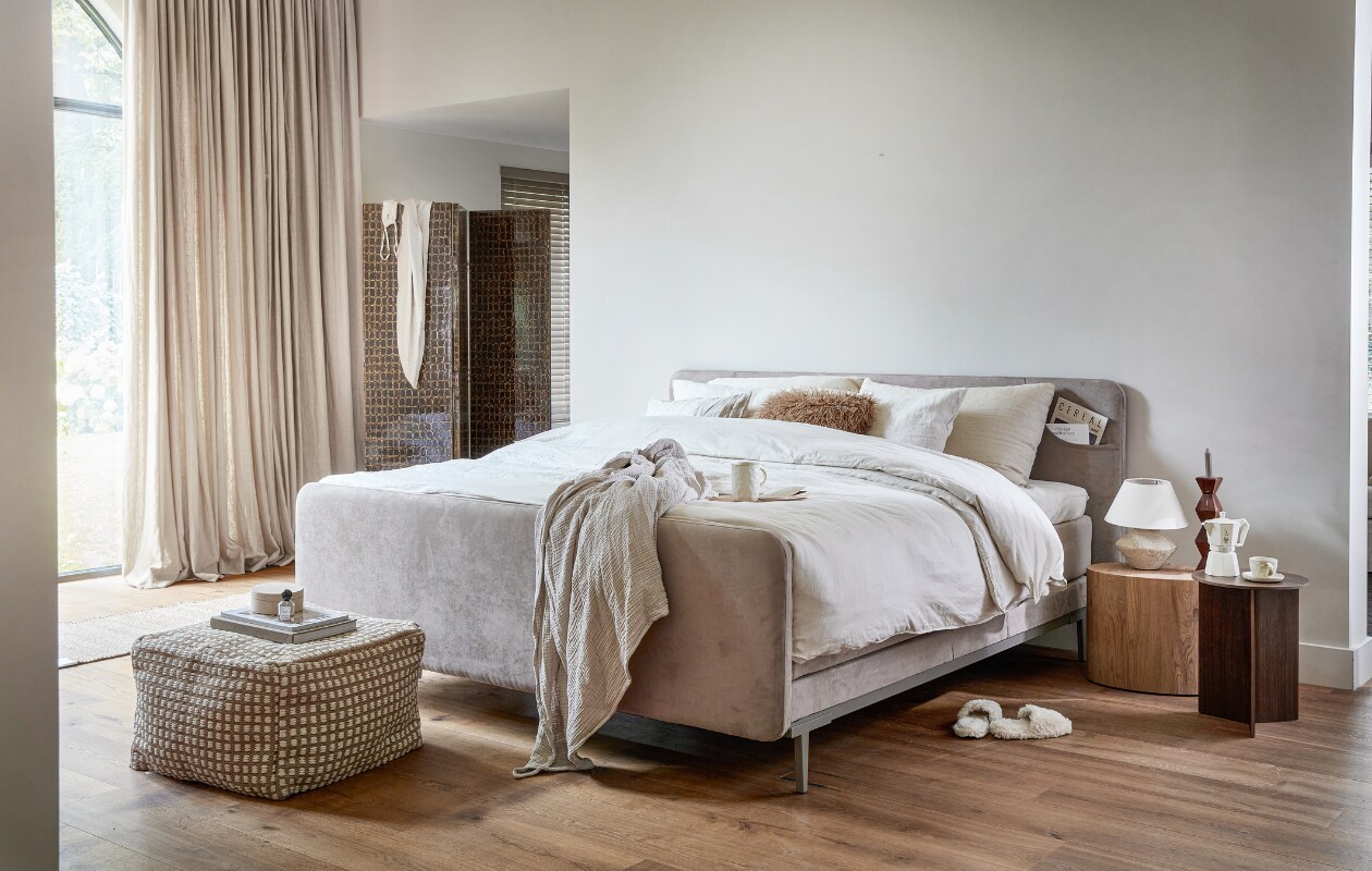 Boxspring Lifestyle by vtwonen Basil, hier in 200x210 cm, vanaf € 1990,-, hier uitgevoerd met elektrisch verstelbare bodem, voetenbord en hoofdbord, in stof Major Liver, met metalen poot Angle in Champagne.M.m.v. vtwonen.nl/shop (houten bijzettafel Bernie van By FonQ, walnoten bijzettafel van Hay, poef van Kave Home), zarahome.com (linnen dekbedovertrekset, linnen kussenslopen, sloffen, tafellamp, kop en schotel, koffiekan, kandelaar), hm.com (plaid, harig kussen, vloerkleed, ronde doos). Overig privébezit. vtwonen 13-2023 | productie Tanja Saarberg | styling Sanne Ketelaar | fotografie Peggy Janssen