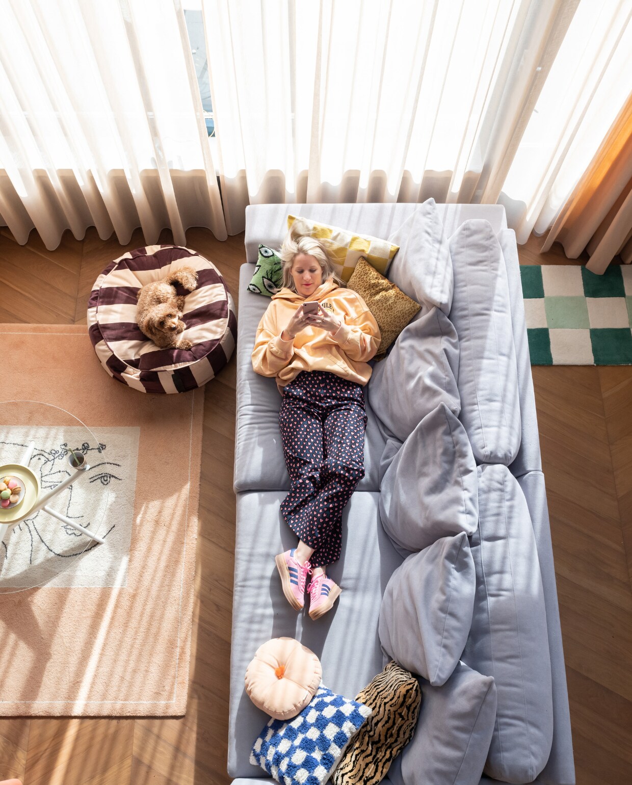 Martine en bezoekhond Sunny in de woonkamer van haar jaren 70 hoekhuis in Vianen. Vloer De Vloeren Kenner. Gordijnen Aan Huis Utrecht.  Picassokleed Marktplaats, salontafel Enter My Attic, schaal Sissy-Boy, wit bord H&amp;M Home. Poef Oyoy Living Design, bank Decor Amsterdam, kussens Sissy-Boy, Tika, Claudi, Noëlle Baartmans en Karwei. Deurmat Jotex. vtwonen special binnenkijken 12-2023 | fotografie Caroline martinot