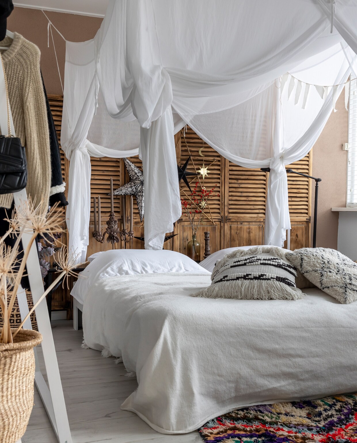 Muurverf Dead Salmon van Farrow &amp; Ball. Bed Auping. Bedhemel Numero74. Shutters, kledingrek, zwarte lamp Marktplaats. Vloerkleed uit Marokko Vinted. Kussens H&amp;M en Karwei. Mand H&amp;M. Plaid El Ramla Hamra. Dekbedovertrek Hema. Kerststerren kringloop, Delight Department, Albert Heijn en Aliexpress. Vaas, paarse kandelaar kringloop. Spiegel Karwei. Sterrenslinger Aliexpress. Overig onbekend. vtwonen 13-2023 | fotografie Henny van Belkom