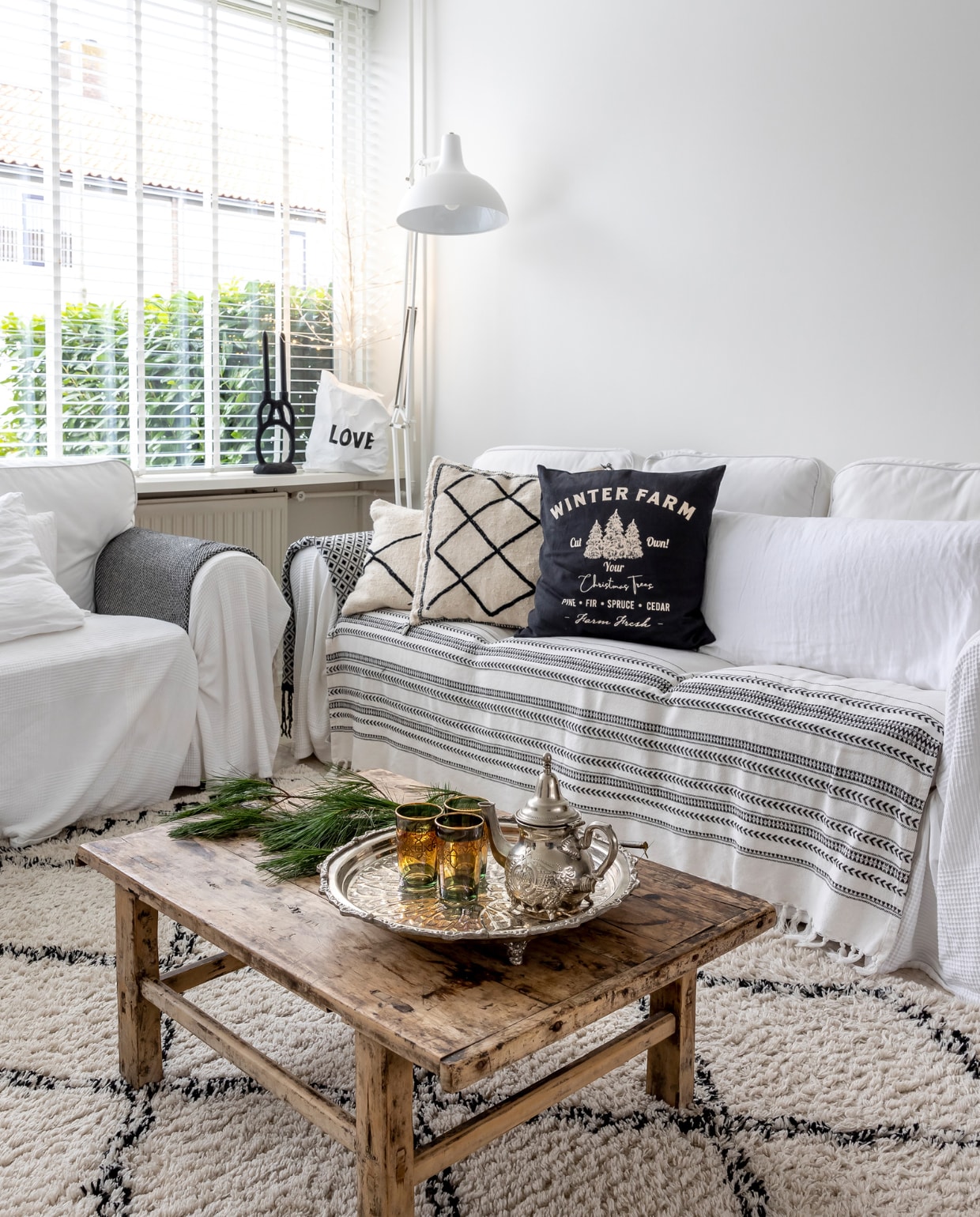 Bank Ektorp Ikea. Salontafel Rockanjeaanzee. Kleed Karwei. Staande lamp Fonq. Zwart-wit kussen uit Marrakech via Vinted. Kussens op bank en gestreepte plaid H&amp;M, witte plaid Ikea. Love tas en kandelaar Loftloft. Theepot en glazen kringloop. vtwonen 13-2023 | fotografie Henny van Belkom