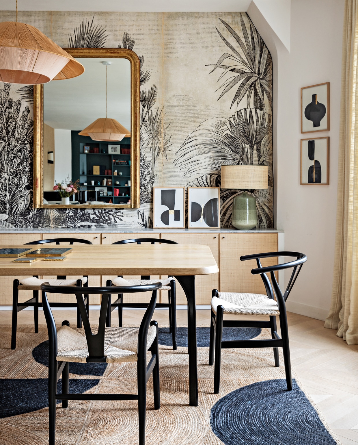Eiken tafel Oasis van Maison Sarah Lavoine. Stoelen Carl Hansen &amp; Søn. Hanglamp Maison Paloma. Spiegel vintage. Behang Le Monde Sauvage. Witte vaas HKliving. Lamp met groene voet Zara Home. Schilderijen Floating House Collection. Vloerkleed Elitis. Overig onbekend vtwonen 12-2022 | styling Marie-Maud Levron | fotografie Yann Deret