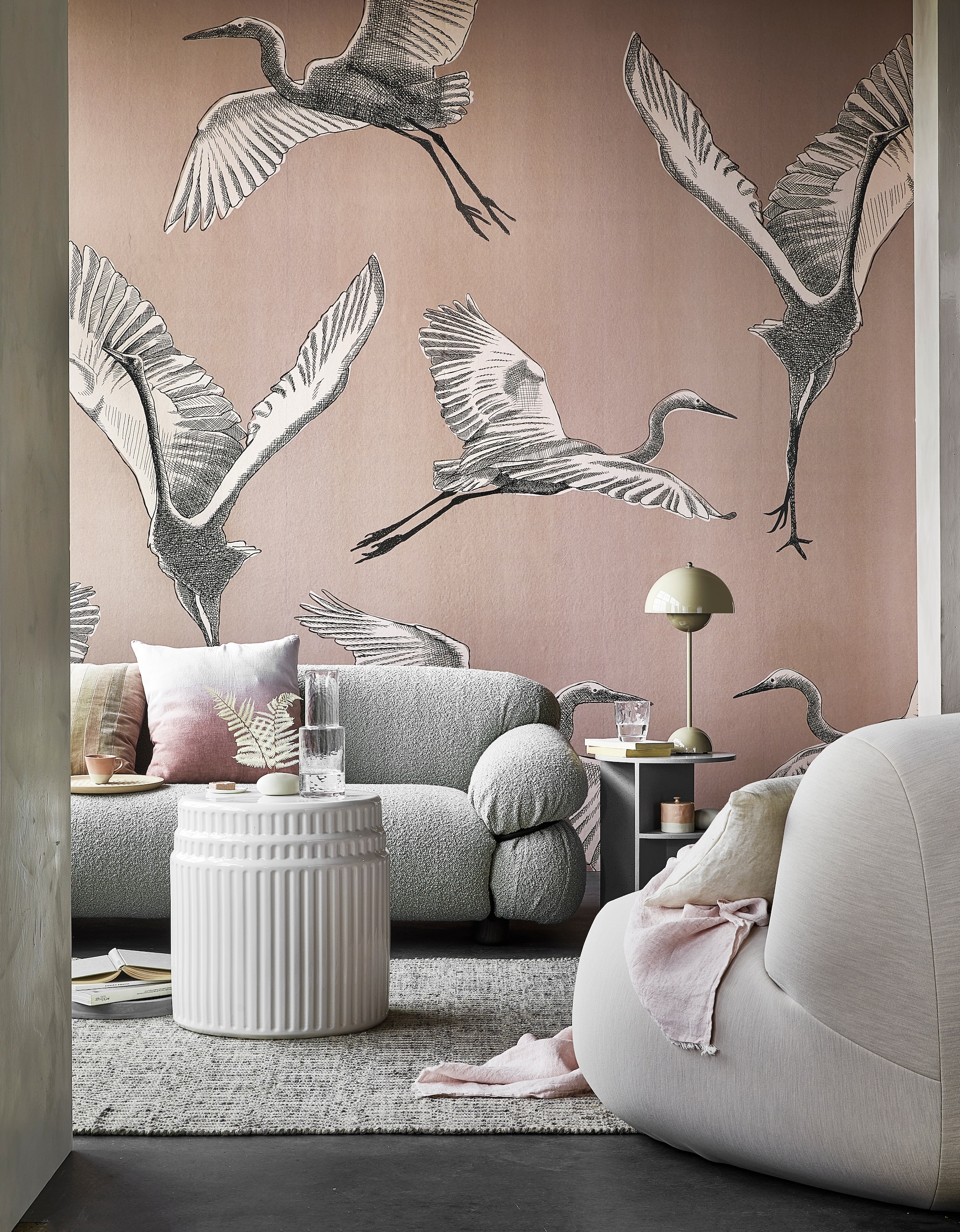 Digitaal behang Graphic Nature, 6 banen van 280x50 cm, totaal (lxb) 280x300 cm € 149,-. M.m.v. kasstoor.nl (bank, kussen met roze kleurverloop, salontafel van wit keramiek, bijzettafel van grijs keramiek, fauteuil), homestede.nl (grijze stenen schaal, houten dienblad, tafellamp), paviljoennoord.com (gestreept kussen, mini-bordje, amberblok), zara.com (kop, karaf, glas, roze pot met deksel), loods5.nl/design (vloerkleed), letoile.store (wit porseleinen vaasje, linnen kussen), bymolle.com (plaid), pure-original.nl (muurverf Fresco in kleur Ashes). Overig privébezit. styling Danielle Verheul | fotografie Peggy Janssen