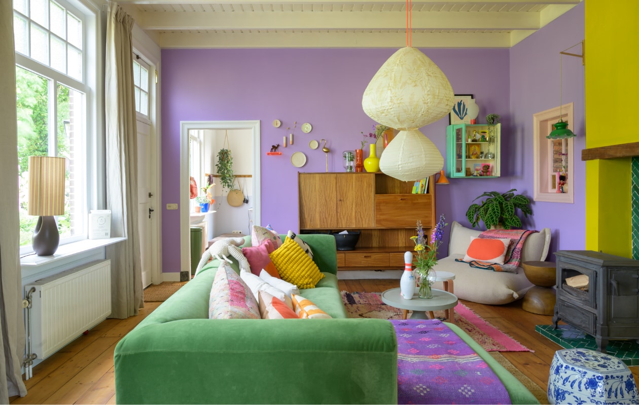 Muurverf paars WO.20.60 van Flexa. Muurverf geel GO.60.60 en verf plafond Ral 9010 van Sikkens. Originele eikenhouten vloer opgeschuurd en behandeld met Osmo Hardwaxolie. Bank HKliving, kussens Ikea, Fatboy, Urban Nature Culture, Van Verre en kringloopwinkel, plaid Van Verre. Vintage kast Marktplaats. Wandkast Van Dijk &amp; Ko. Zitzak Fatboy. Bijzettafels Loods 5, Kleine Gelukjes en Urban Nature Culture. Kruk TipToe, kegel Vintage Friends, vaas Urban Nature Culture. Hanglampen HKliving. Vloerkleden Evenaar en Wanderwood. Kachel Efel. Overig onbekend. vtwonen special binnenkijken 121-2023 | fotografie Trui Heinhuis