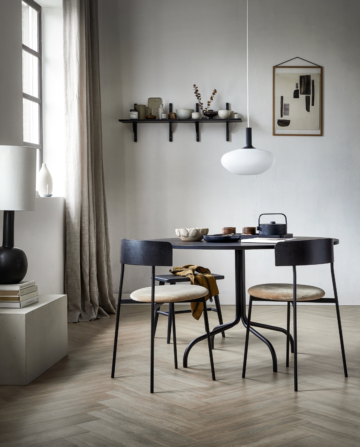 Laminaatvloer visgraat Rafter, lamel 65,5x13,3x0,8 cm, met groef, per m²  € 34,99. M.m.v. vtwonen.nl/shop (wandplanken van Ferm Living, hanglamp Nordlux, theepot, houten theekop en zwart dienblad van Serax), festamsterdam.com (eettafel Friday, eetkamerstoel Friday), sissy-boy.com (beige schaal met reliëf), @studio__yen (tafellamp), pantoufle-design.nl (kandelaar in vensterbank, witte kommen op wandplank), thefinestore.com (beige dienblad, koffiekan), facade-apt.com (print), aedamanthony.nl (houten lijst), zarahome.com (witte vaas). Overig privébezit. vtwonen 01-2024 | productie Tanja Saarberg | styling Kim van Rossenberg | fotografie Sjoerd Eickmans/Peggy Janssen