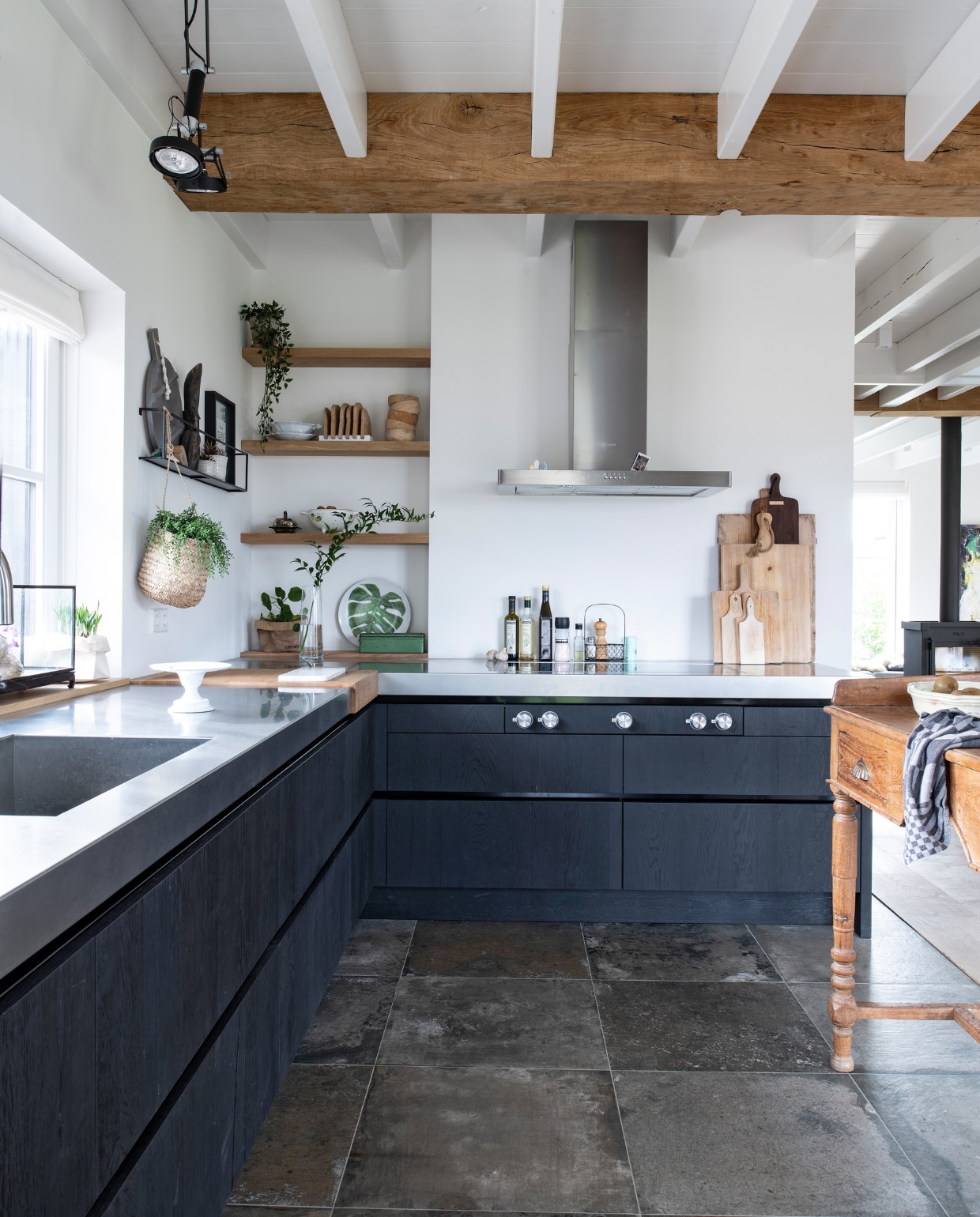 Keuken met rvs-werkblad Buro Logge, \ taartplateau kringloop, hangplant Loods 5, houten planken aan de muur en houten snijgedeelte Böhmer Project. Bord met blad Action, afzuigkap Smeg, houten snijplanken Dutchdeluxes en Kitchen Trend. Muurrek Woood met daarin een Afrikaans beeldje gekocht op een markt in Kenia, fotolijst Atelier Sukha. Houten bakjes, ronde plank en kleine snijplanken HKliving. vtwonen 13-2020 | productie Insidehomepage | styling Marlies Does | fotografie Louis Lemaire