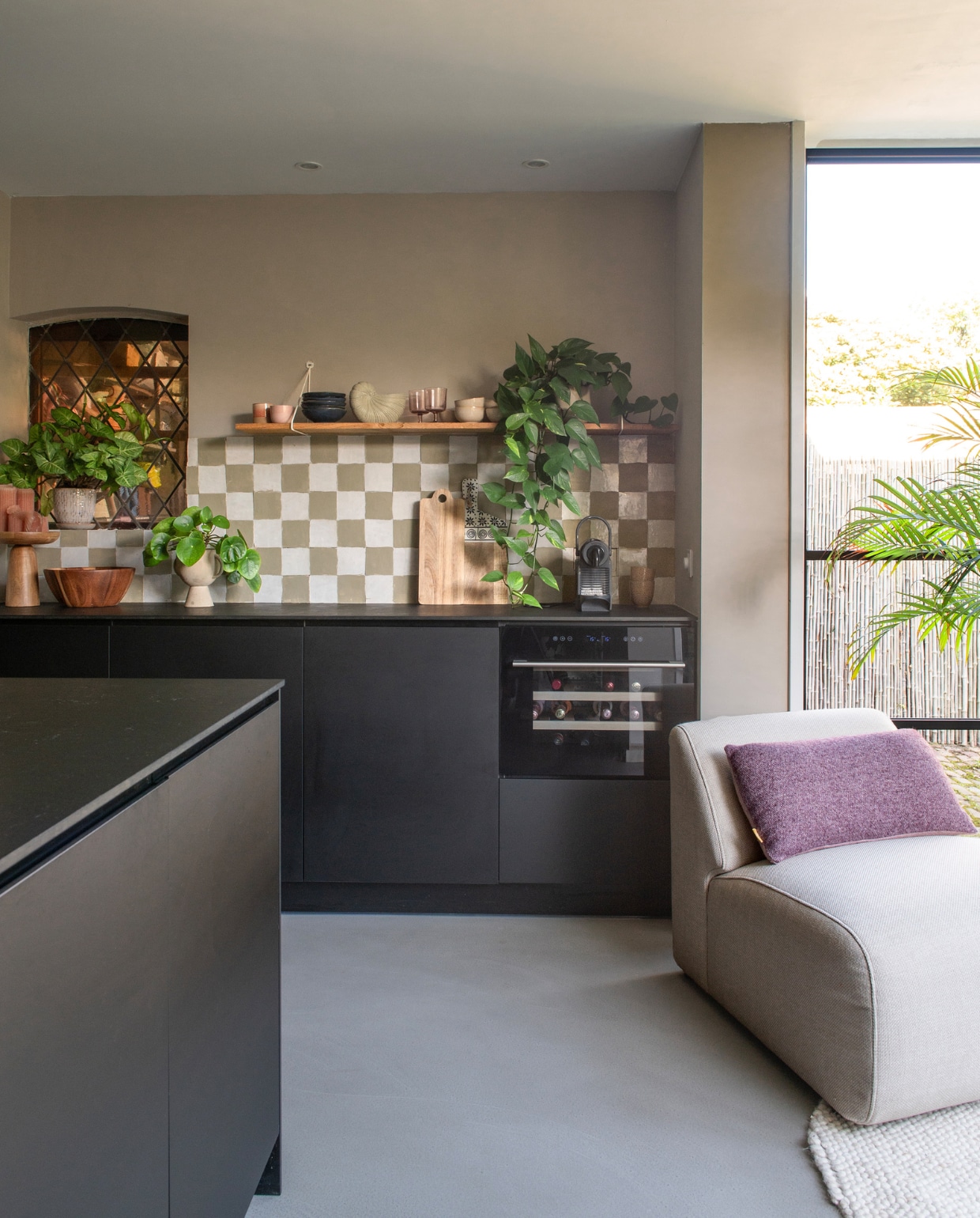 Keuken Kvik, Witte Marokkaanse zelliges Designtegels, groene tegels geschilderd in Limited Jade van Lab Paint. Fruitschaal Dille &amp; Kamille, verhoogd plateau Sissy-Boy, fauteuil Zuid Amersfoort, kussen de Bijenkorf, vloerkleed Trendcarpet, muurverf Mushroom van Lab Paint, schelpenvaas Bokker geschilderd in Limited Jade van Lab Paint, blauwe schaaltjes Casa, glazen Hema, planten Intratuin, topvloer woonbeton van Coatingvloer.nl. Overig onbekend. vtwonen 01-2024 | productie De Binnenkijkers | styling Jeske Weel | fotografie Caroline Coehorst