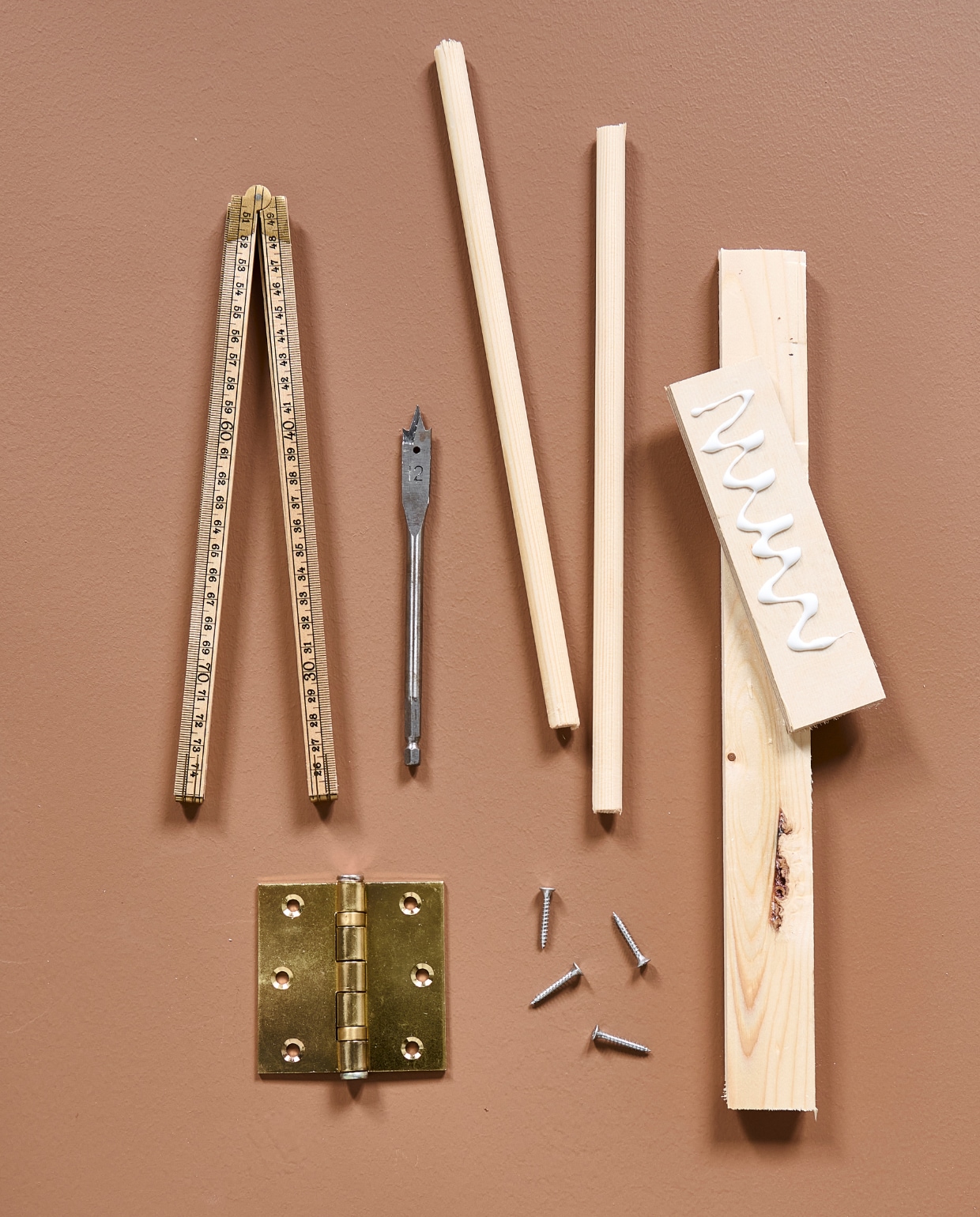 Benodigdheden voor het droogrek, te zien is: kogelscharnier, schroeven, vuren lat met houtlijm, grenen ronde stokken, houtboor en meetlat. vtwonen special DIY 8-2024 | styling Kelly van Gendt, Corrien Flohil | fotografie Sjoerd Eickmans
