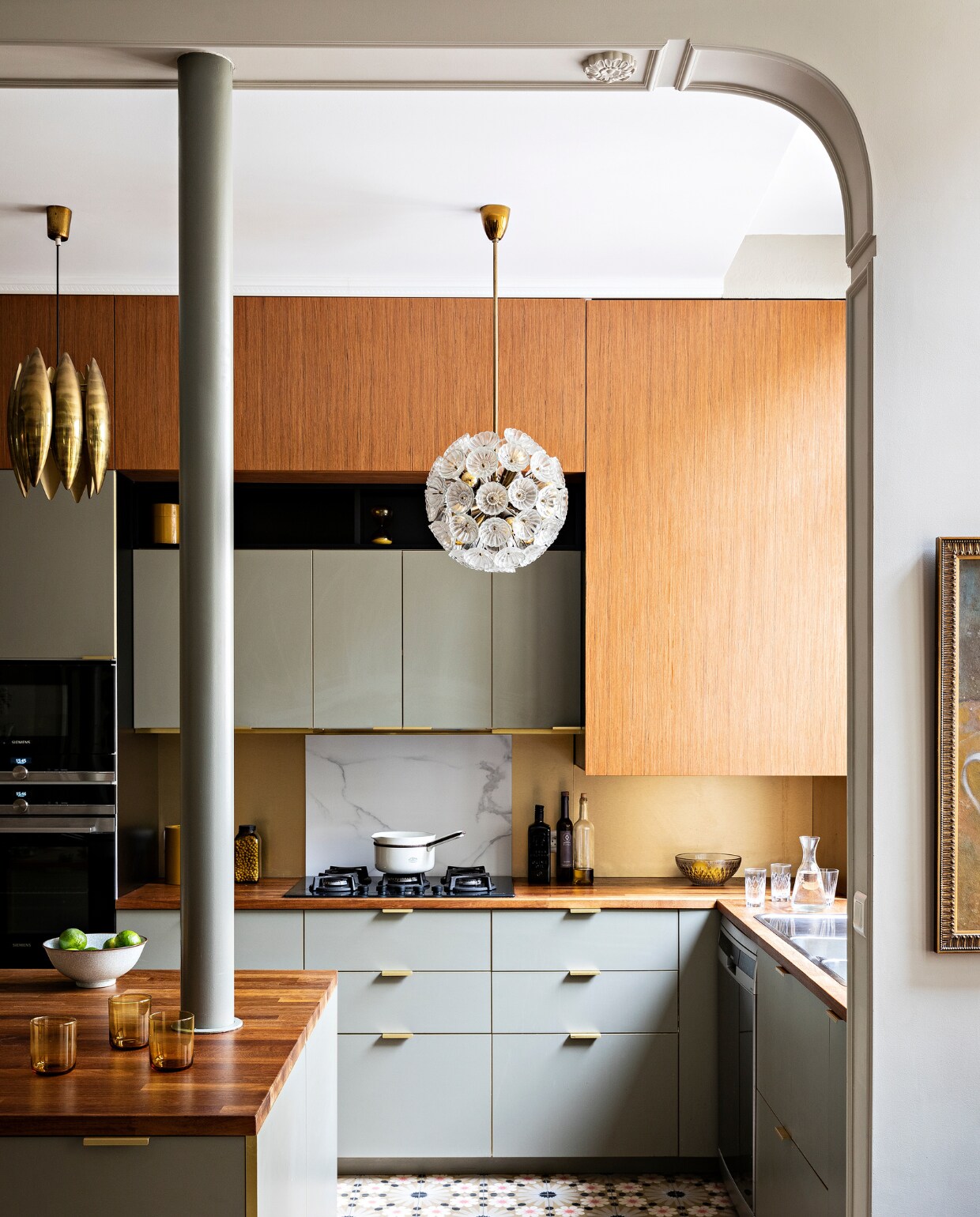 Basiskeuken Ikea, deurtjes en grepen Bocklip, teakhouten werkblad Ixana, teakhouten bovenkasten Dispano. Messing Florence Knoll-hanglamp en glazen Emil Stejnar-hanglamp   vintage. Overig onbekend. vtwonen special binnenkijken 3-2022 | Productie AC Scoffoni | Styling Marie-Maud Levron | Fotografie Yann Deret