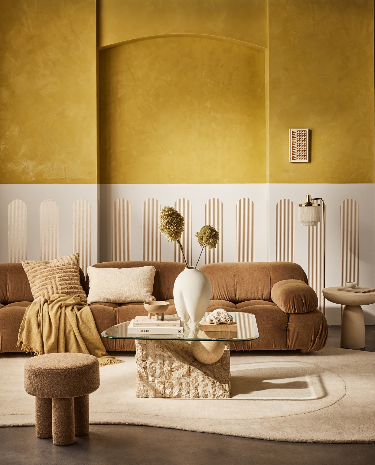 vtwonen collectie (behangstrook Streep Gold-Egg White, 17,6 cm (b), rol van 10 m). M.m.v. homestede.nl (bank, kussens, plaid), edha-interieur.nl (poef, bijzettafel), goeds.nl (vloerkleed van Layered, lamp), pietjonker.nl (salontafel), rollmannceramics.com (kunsttegel), lauthentique.nl (kalkverf gele muur Korengoud, krijtverf witte muur Krijt), 101cph.com (vaas, schaal). Overig privébezit. vtwonen 02-2023 | productie Tanja Saarberg | styling Cleo Scheulderman | fotografie Jeroen van der Spek