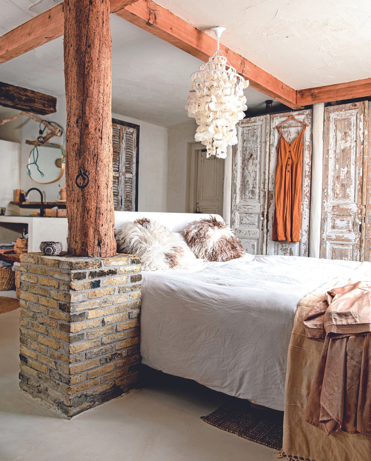 Vloer StucDeco met drie lagen vernis en leemstuc op de wand van Ecowonen. Wandlamp zelfgemaakt, spiegel Loods 5. Kastdeuren Burbri, dekbedovertrek H&amp;M Home, kimono kringloop, jurk Zara, kussens De Zeekraal. Schelpenlamp souvenir uit Brazilië. Overig onbekend. vtwonen 02-2024 | productie Inside Homepage | styling Esther Loonstijn | fotografie Louis Lemaire