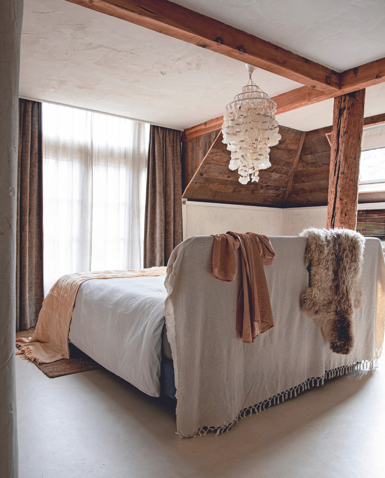 Schapenvacht De Zeekraal, plaid kringloop. Dekbedovertrek en vloerkleed H&amp;M Home. Visschubbenlamp souvenir uit Brazilië. Gordijnen en vitrage Karwei. Vloer StucDeco met drie lagen vernis en leemstuc op de wand van Ecowonen. De paal is een wrakstuk. vtwonen 02-2024 | productie Inside Homepage | styling Esther Loonstijn | fotografie Louis Lemaire