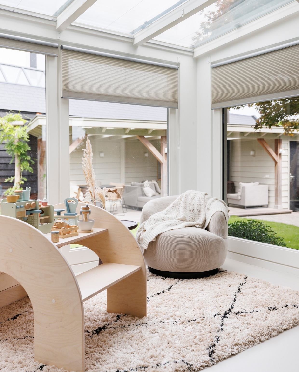 Vloerkleed, plaid en fauteuil Basiclabel. Plisségordijnen Van Besouw, klimboog FitWood, houten speelgoed Little Dutch, pampaspluimen Leen Bakker. Buiten: pergola Janse &amp; Berkhof Tuinen, verf pergola Shadow White van Farrow &amp; Ball, tuintegels Vida waalformaat, tegels onder pergola GeoCeramica, loungeset Exotan. Salontafels en wanddecoratie By-Boo. Tafelhaard Cosi Fires, wandlampen Rietveld Licht. vtwonen 03-2024 | Fotografie Margriet Hoekstra