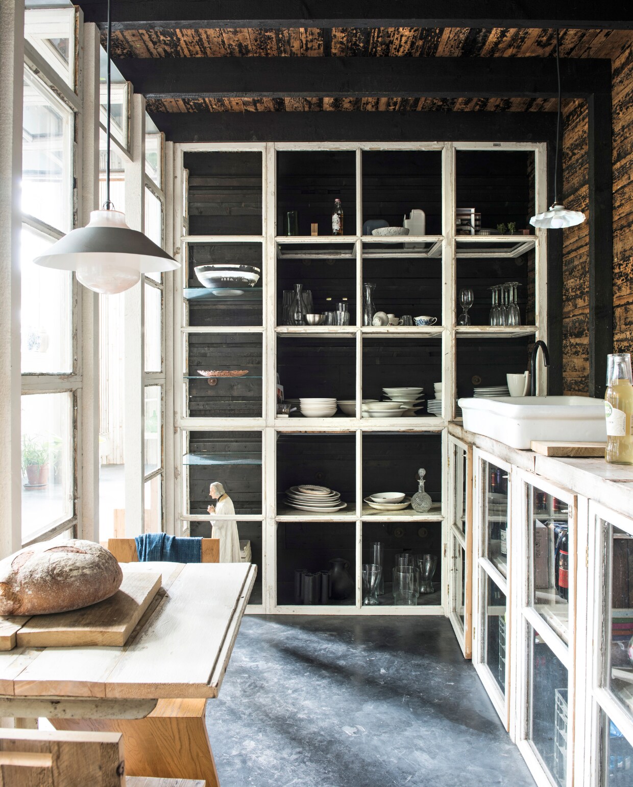 De keuken grenst aan het woongedeelte en is afgesloten met oude houten raamkozijnen uit de barak. Lamp links van Klaas Kuiken &amp; Dieter Volkers, lamp rechts van de brocante. Tafel van Niek Wagemans, stoel van Gerrit Rietveld. Broodplank is een eiken plank. De spoelbak komt uit het huis van Rolf en Yffi in Frankrijk, kraan van Ikea. Tegen de muur zit dakbeschot met teer. De schaal linksboven is gemaakt van restjes kunsthars, onder andere restjes van de Knotted Chair van Marcel Wanders, en gemaakt door Wandschappen. vtwonen 03-2017 | Styling Inge van Lieshout | Fotografie Louis Lemaire/Insidehomepage