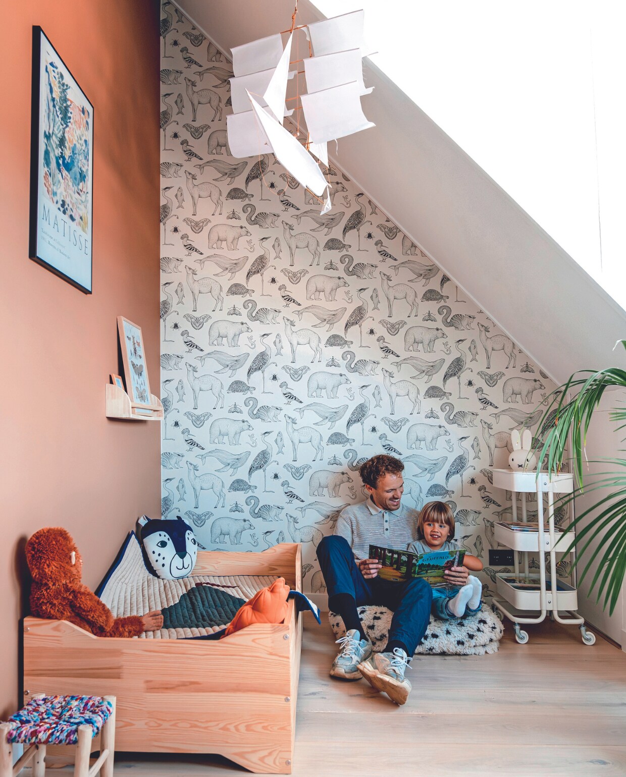 Muurkleur Dandy Dust van Flexa, behang Ferm Living, eiken parketvloer Multiplank van Laminaat en Parket, lijst Desenio, poster Matisse, boekenplank Zara Home, lijst erop Postery, kruk Le Petit Nomade, kinderbed Petit Puk, beddengoed Crisp Sheets, sprei Ferm Living. Aap en trolley Ikea. Knuffelkussen Nobodinoz, kussen oranje blad H&amp;M Home, zeilschip Haptic Lab via Ziloen, poef Studio Pure, lamp Nijntje Mr Maria, plant Kentiapalm. Overig onbekend. vtwonen 02-2024 | fotografie Myrthe Slootjes