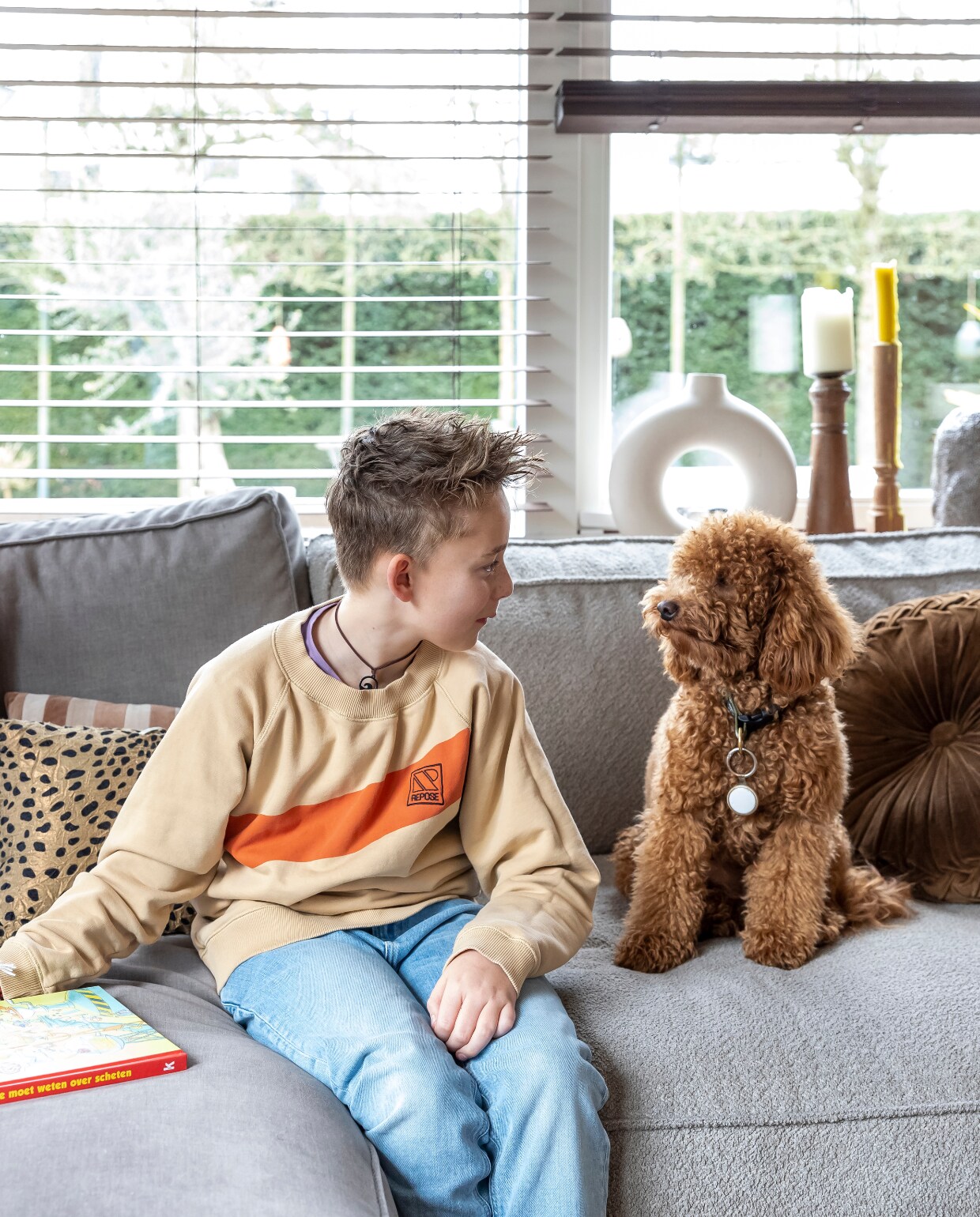 Tyler op de bank in de verbouwde boerderij. Kandelaars in vensterbank HKliving en Loft. Bank Melchior Interieur, kussens Ferm Living en HKliving. vtwonen 02-2023 | styling Karin van Schie | fotografie Henny van Belkom