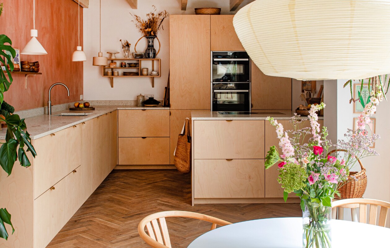 Muurverf Chalky Coral van Pure &amp; Original. Vloer van gebruikt hout De Oude Plank. Keuken gebouwd door Justustjebbo, terrazzo aanrecht Maarten Zwartjes, kraan Quooker, ovens Neff. Wandrek Woodchuck, keramiek in en op wandrek o.a. Rosa de Weerd. Schaal Atelier Hop, grote vaas erfstuk van oma, mand op kast H&amp;M Home, vintage mand in hoek kringloop. Prints aan de muur Eva Offredo. Boodschappentas H&amp;M Home. Hanglampen NM Design en Liewood. Overig onbekend. vtwonen special binnenkijken 121-2023 | productie De Binnenkijkers | styling Jeske Weel | fotografie Caroline Coehorst