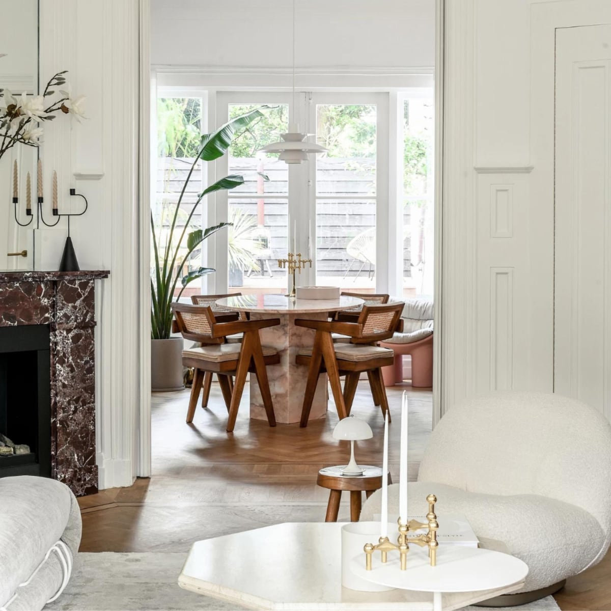 Eettafel en schouw van burgundy-marmer Stoned. Stoelen en houten kruk Detjer. Witte hanglamp PH5 en oplaadbare tafellamp Panthella van Louis Poulsen. Hanglamp met bollen Amazon. Kandelaar op schouw Ferm Living. Fauteuil Gubi. Salontafel vintage. Gouden kandelaar op voorgrond Stoff. Witte bijzettafel &amp;Tradition. Overig onbekend. vtwonen 1-2023 | styling &amp; fotografie Ellis &amp; Michiel